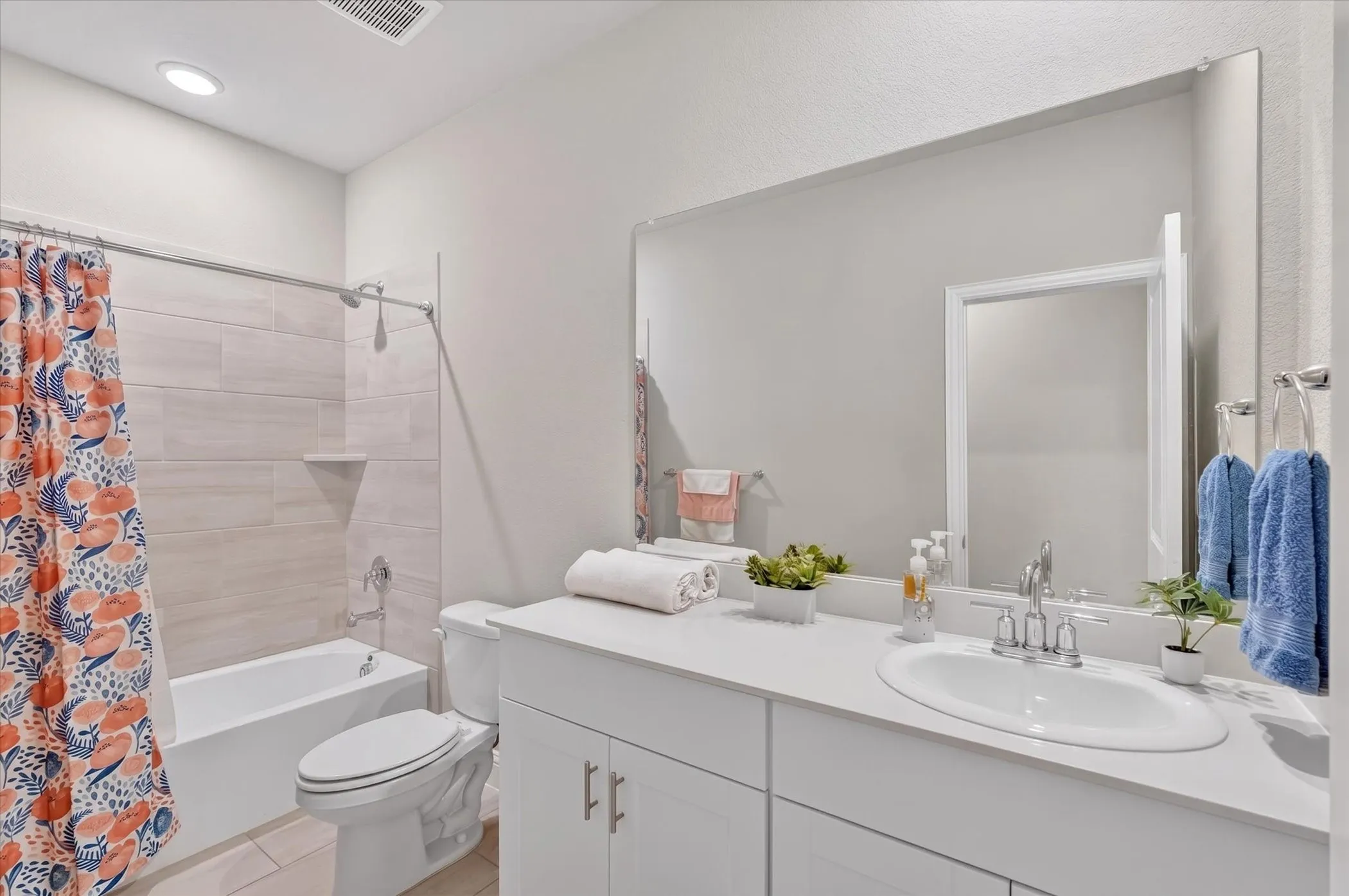 Bathroom featuring a white vanity with an undermount sink, a large wall-mounted mirror, a built-in tub with a shower, and light-toned horizontal tile surrounding the tub