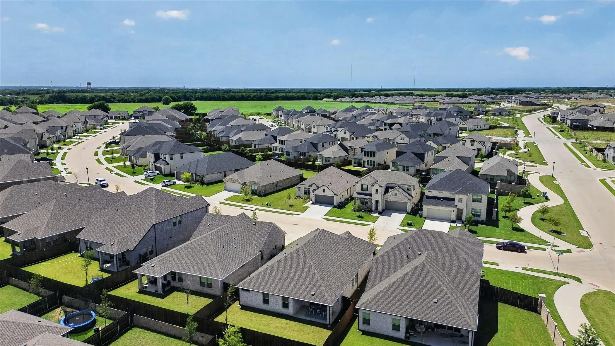 Residential neighborhood featuring numerous single-family homes with gray shingle roofs, manicured lawns, and paved roads