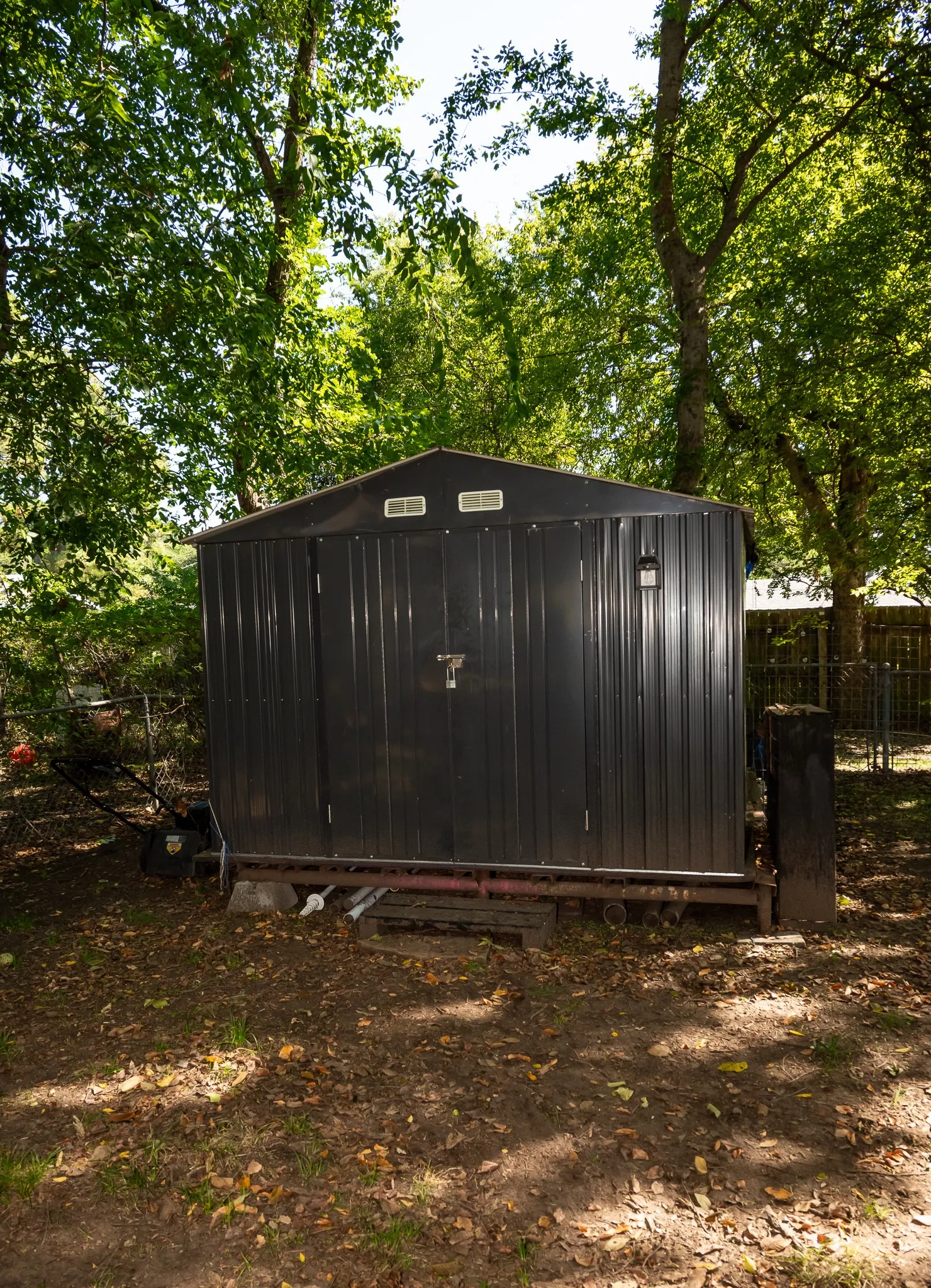 Dark-toned metal storage structure featuring dual doors and dual gable vents, set upon an elevated steel frame foundation