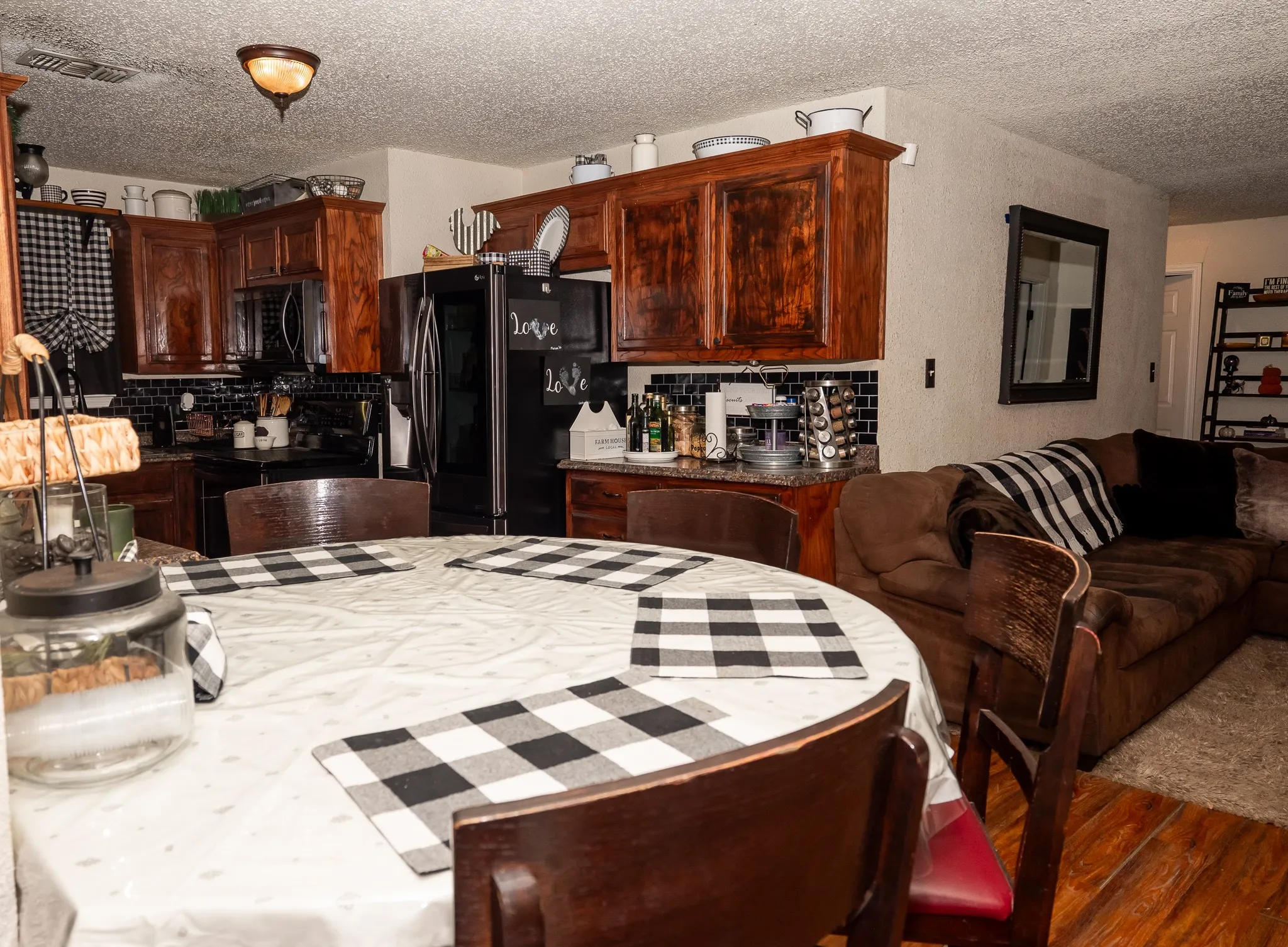 Kitchen featuring stained wood cabinetry, black subway tile backsplash, and dark stone-finish countertops, accompanied by wood-finish flooring