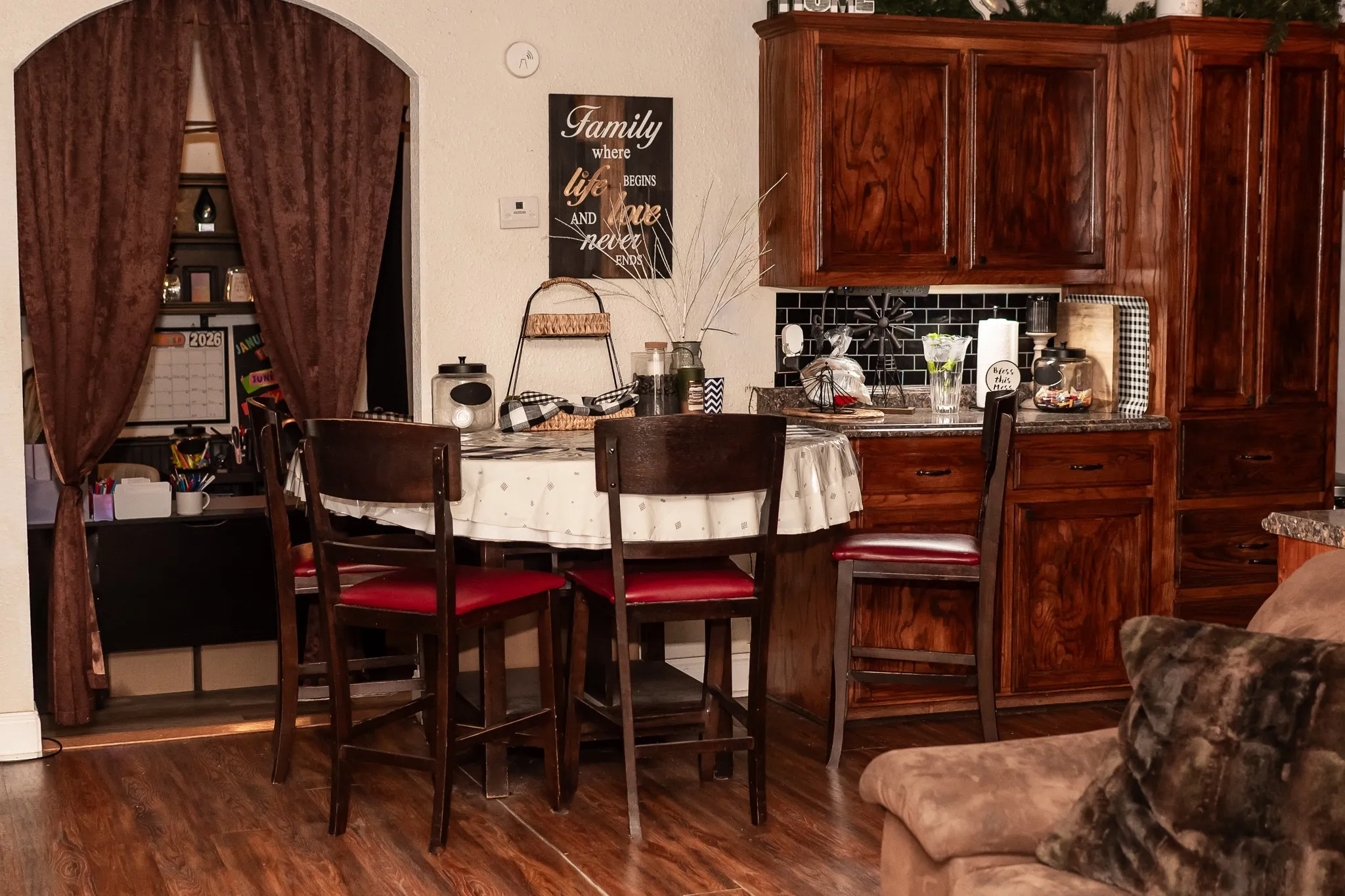 Stained wood cabinetry, black subway tile backsplash, arched doorway, and wood-finish flooring