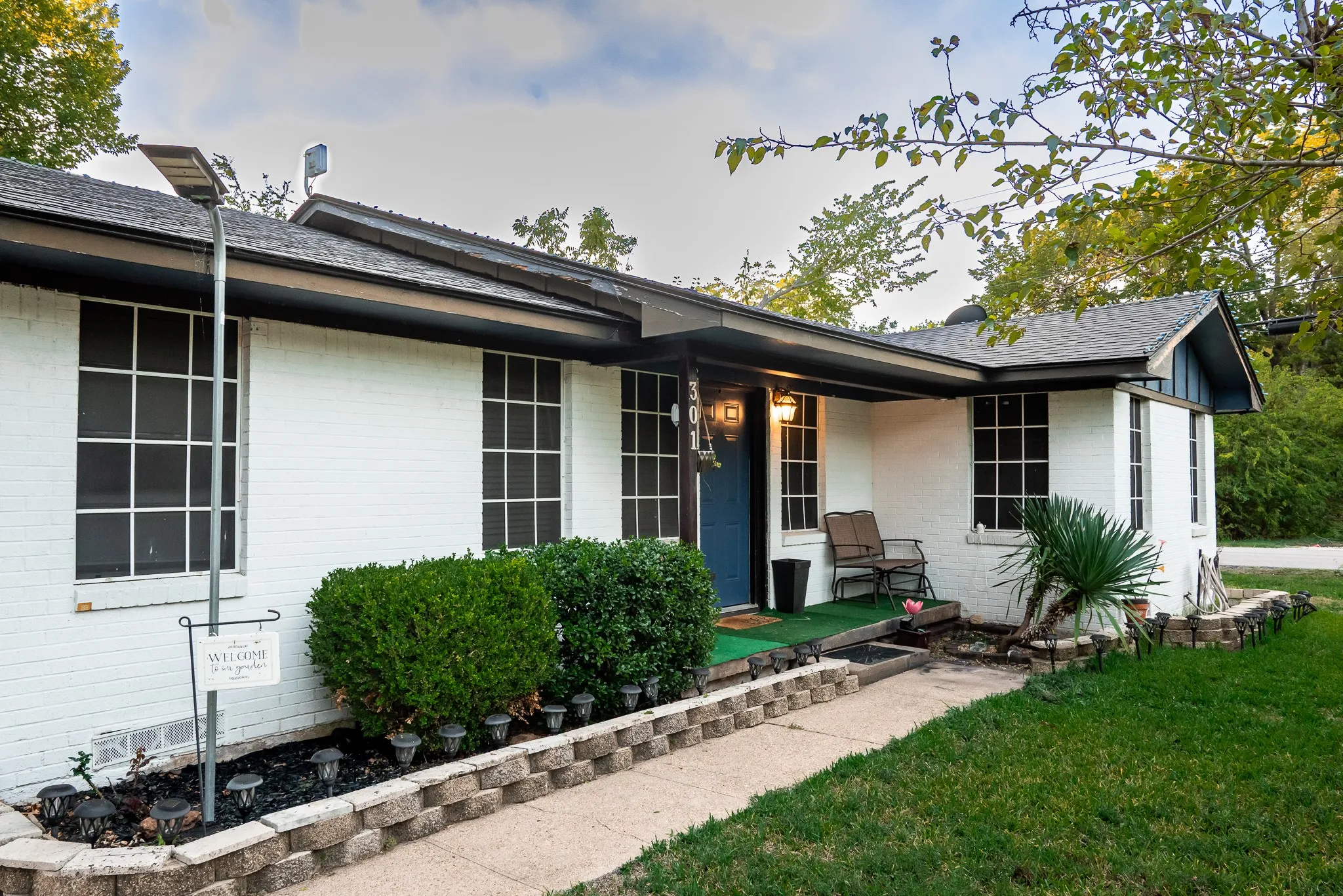 Painted brick exterior featuring a covered front porch, multi-pane windows, a concrete walkway, and stone-block garden edging
