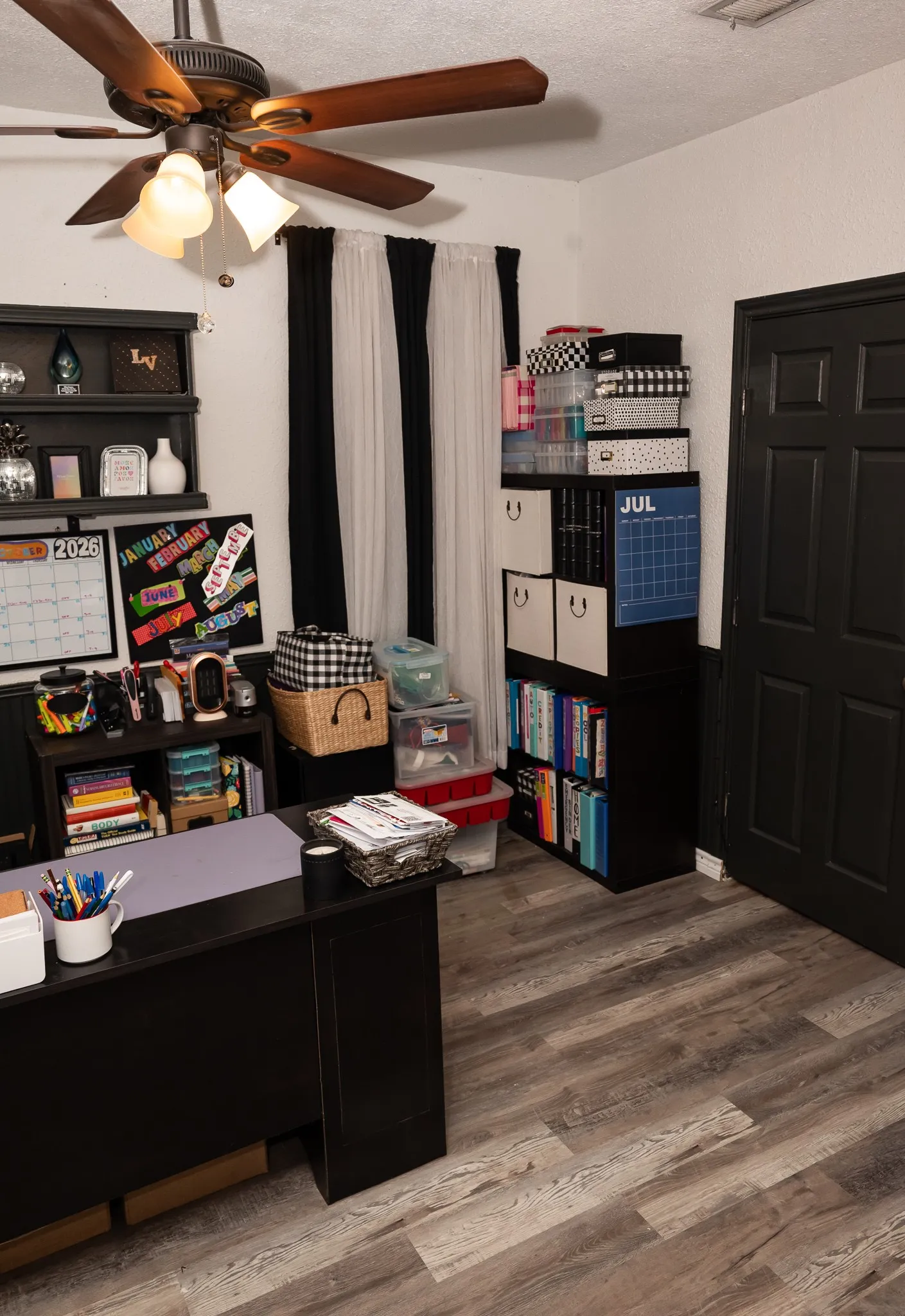 Wood-finish flooring, ceiling fan with integrated lighting, and a six-panel door with a dark finish