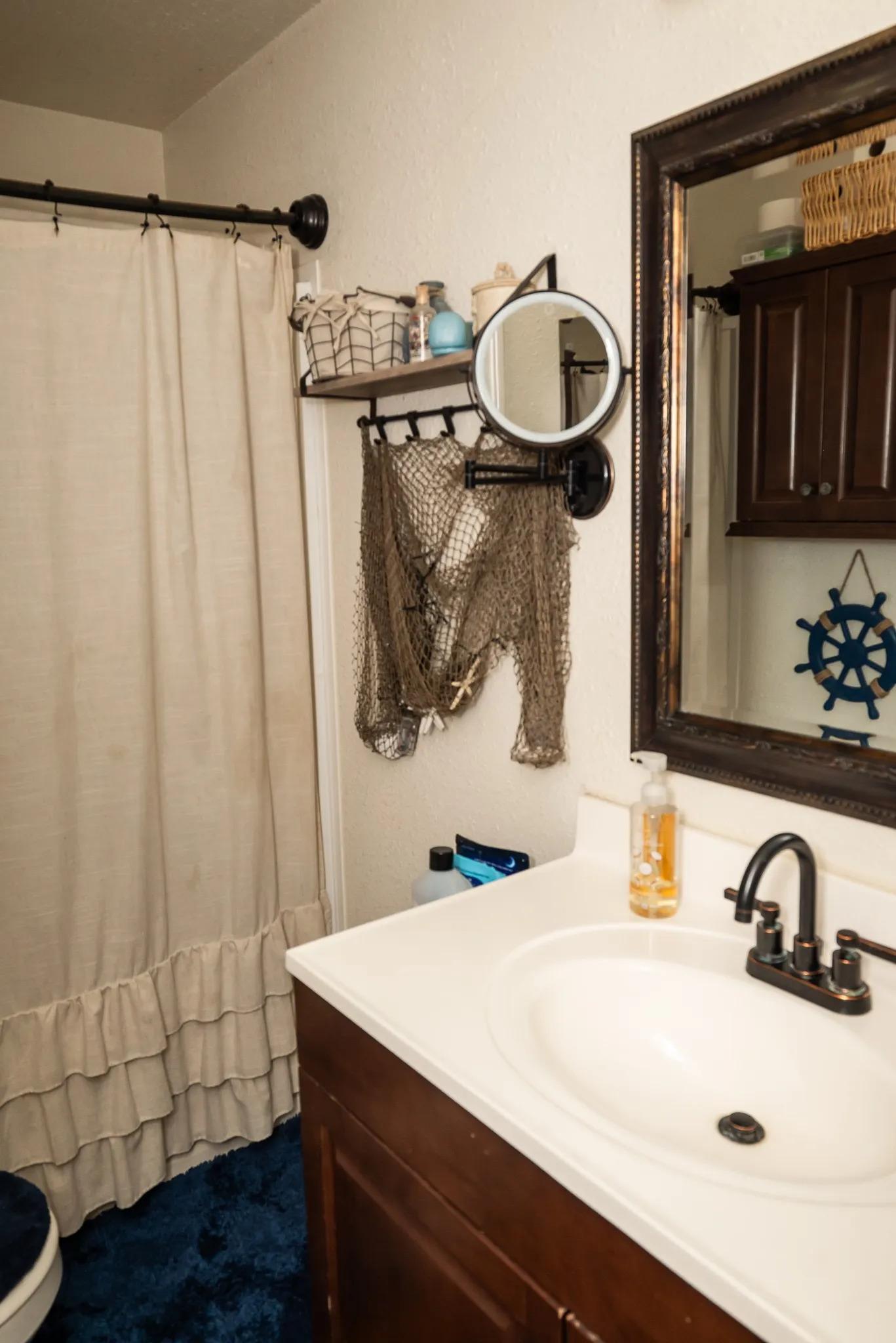 Dark wood vanity with a white countertop and oval undermount sink featuring an oil-rubbed bronze dual-handle faucet, wall-mounted adjustable mirror, and a framed mirror above the vanity
