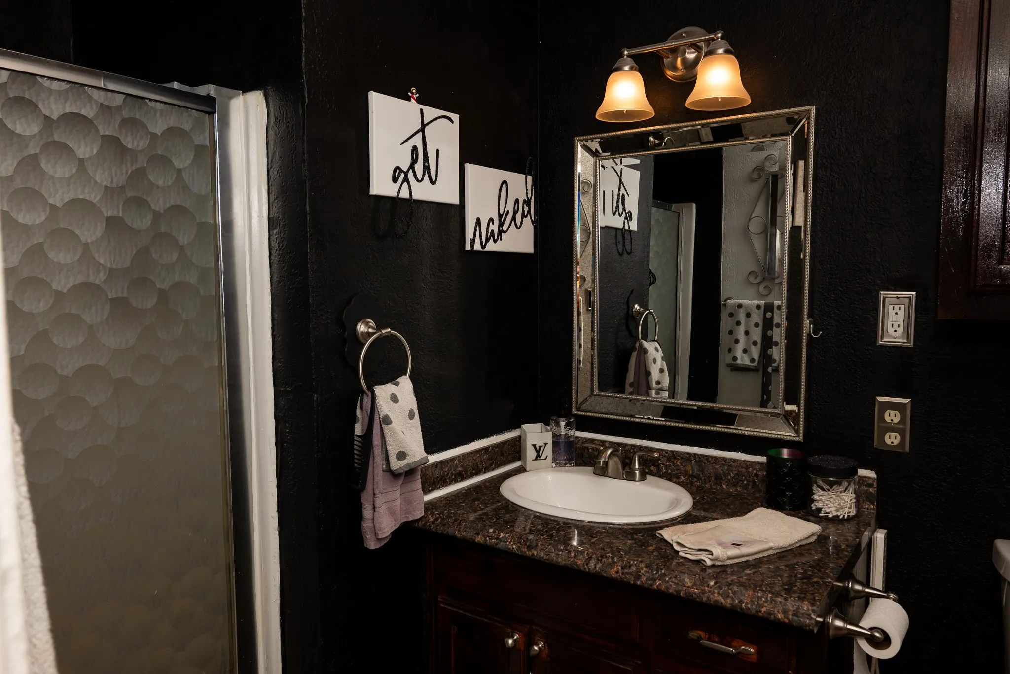 Bathroom featuring a vanity with a stone-finish countertop, undermount oval sink, dual-light wall-mounted fixture, and a framed mirror