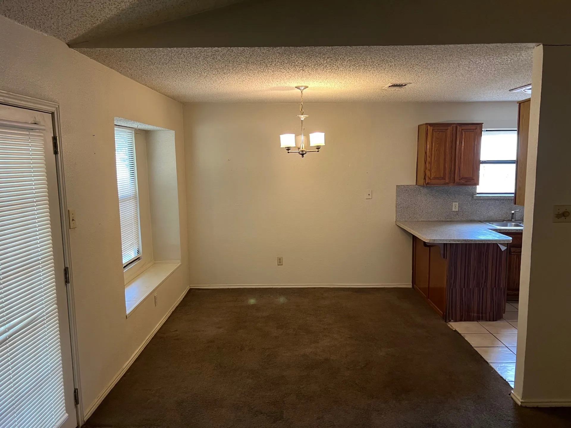 Carpeted dining area featuring a chandelier, a built-in window seat, and access to a kitchen with wood-finish cabinetry and a bar-height counter