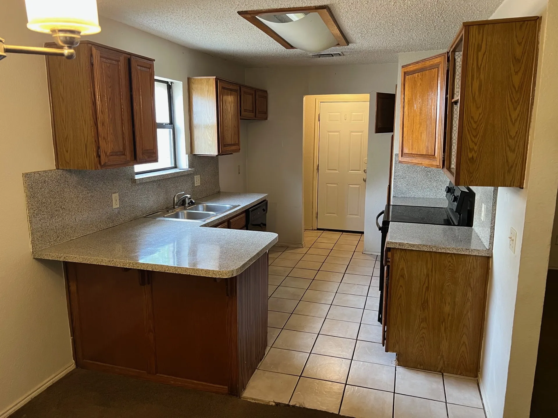 Kitchen featuring wood cabinetry, light-toned countertops, a double basin sink, and tile flooring