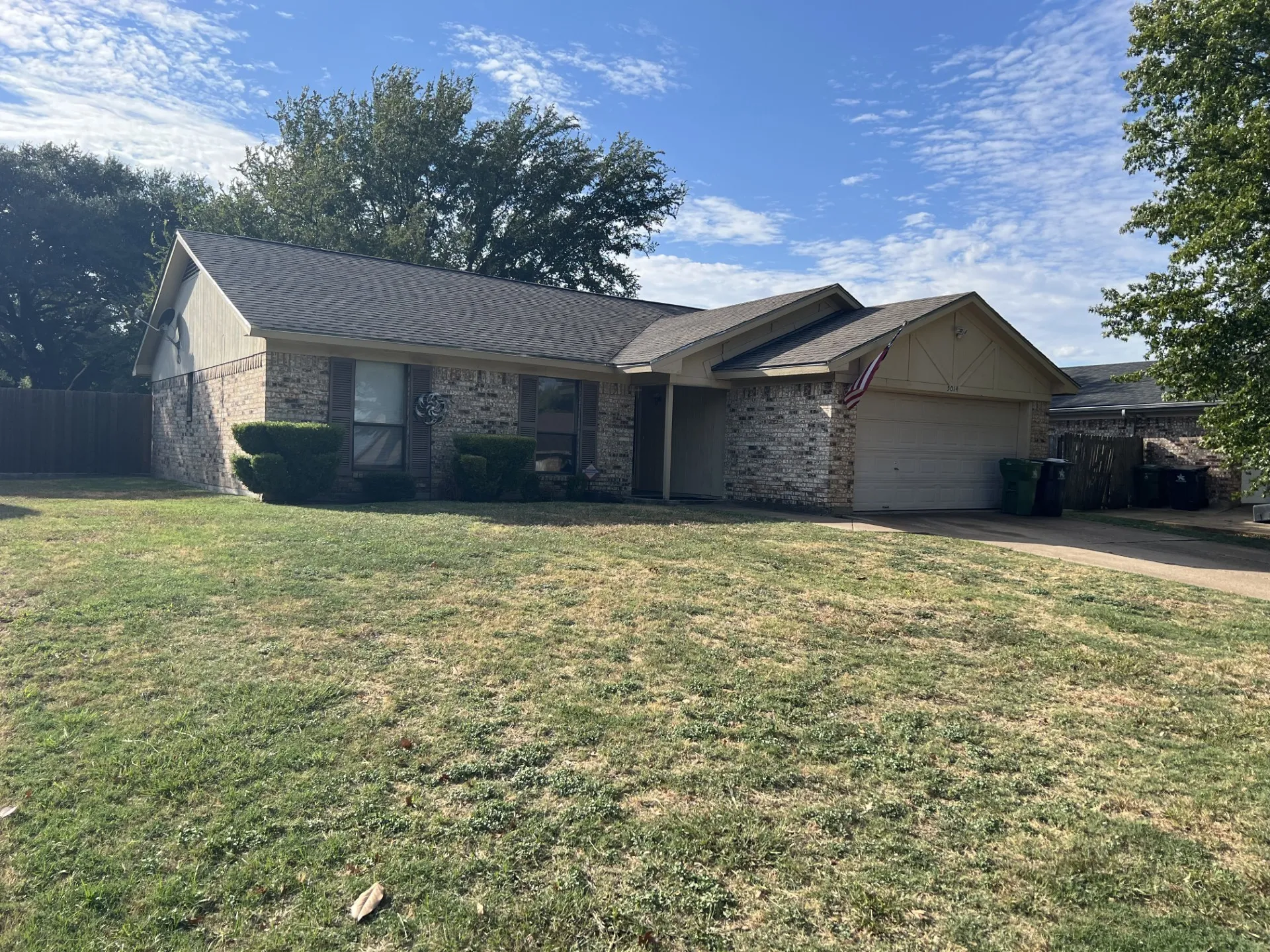 Brick and stucco exterior with an attached garage, featuring a shingled roof and mature landscaping