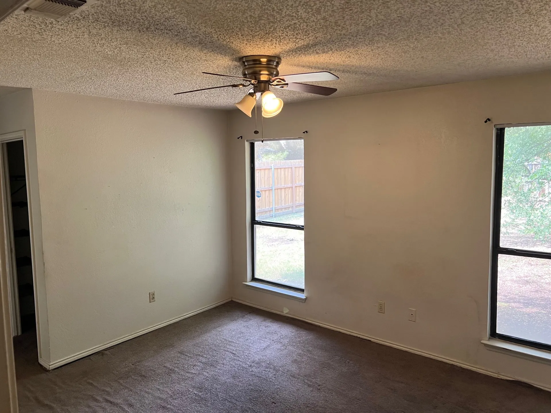 Ceiling fan with integrated lighting, two windows with dark frames, and carpeted flooring