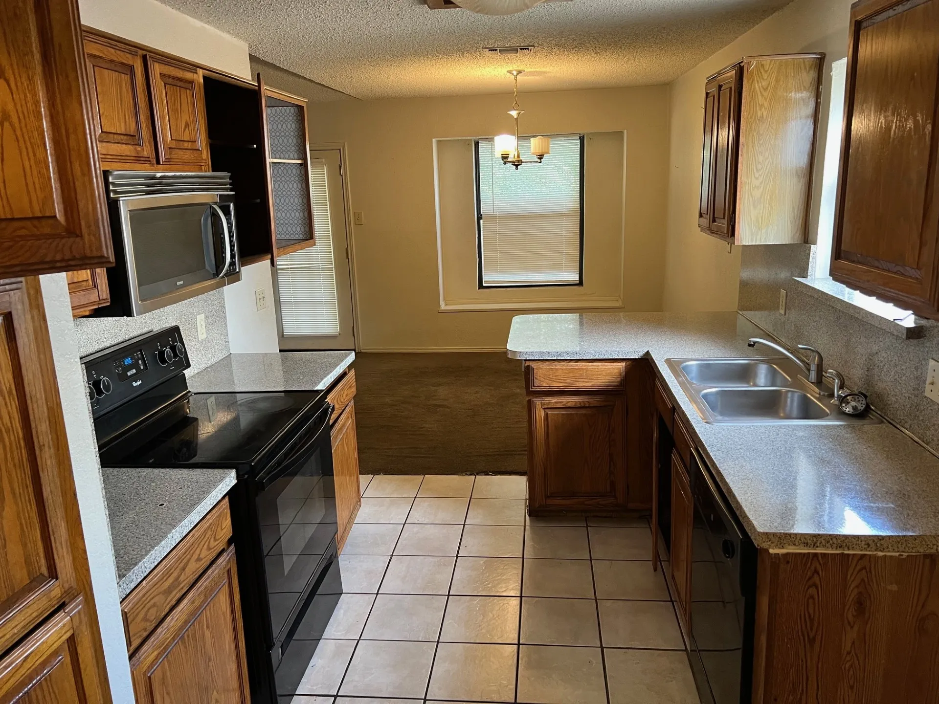 Kitchen featuring wood cabinetry, stone-finish countertops, stainless steel microwave, black electric range, and a double basin stainless steel sink