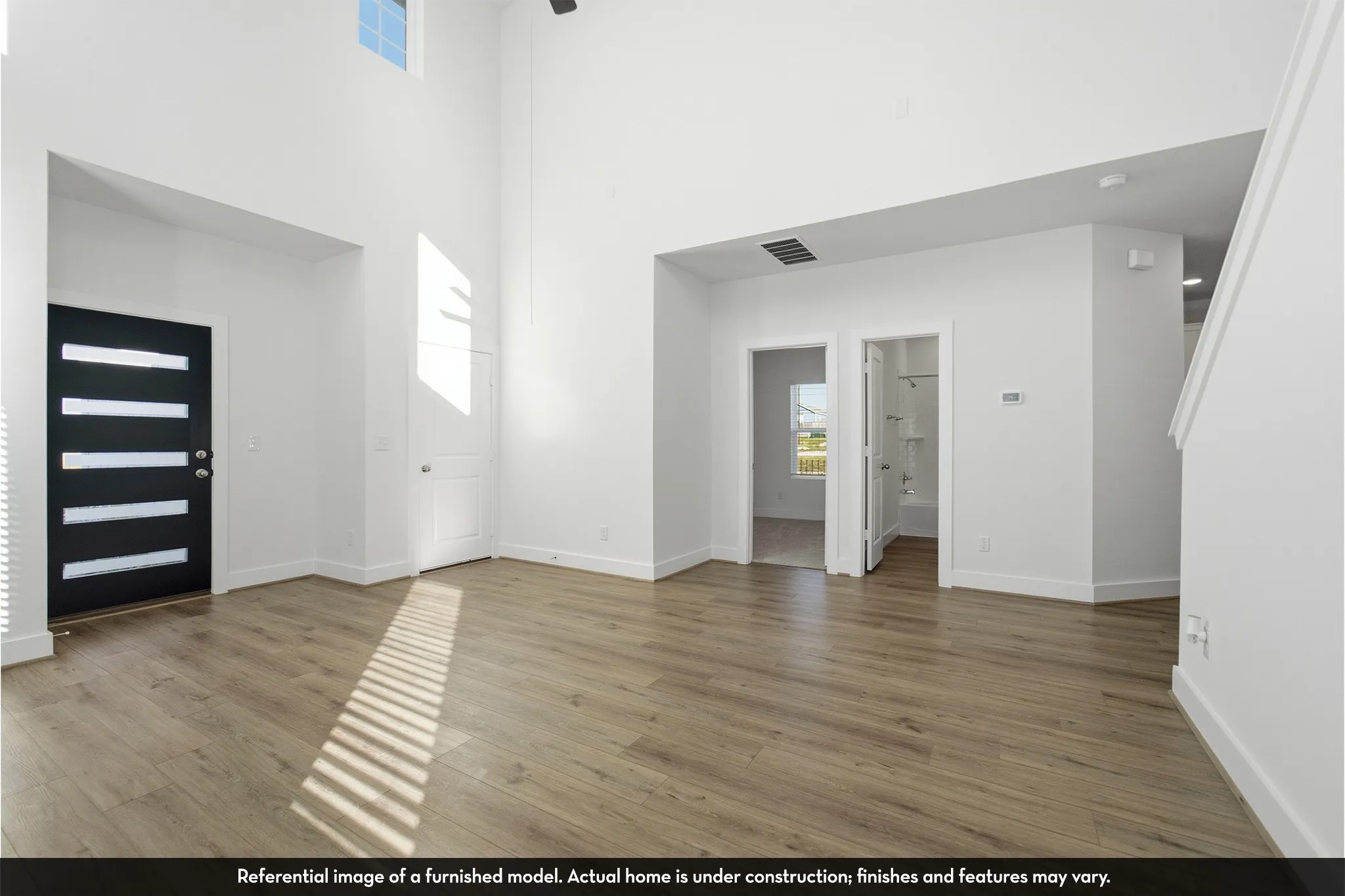 Double-height ceiling, wood-finish flooring, and modern entry door with horizontal frosted glass inserts