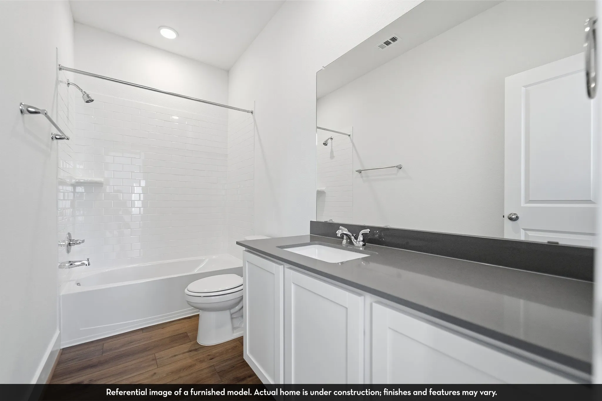 Bathroom featuring a white vanity with a dark gray countertop, an undermount rectangular sink, wood-finish flooring, and a tub-shower combination with white subway tile surround