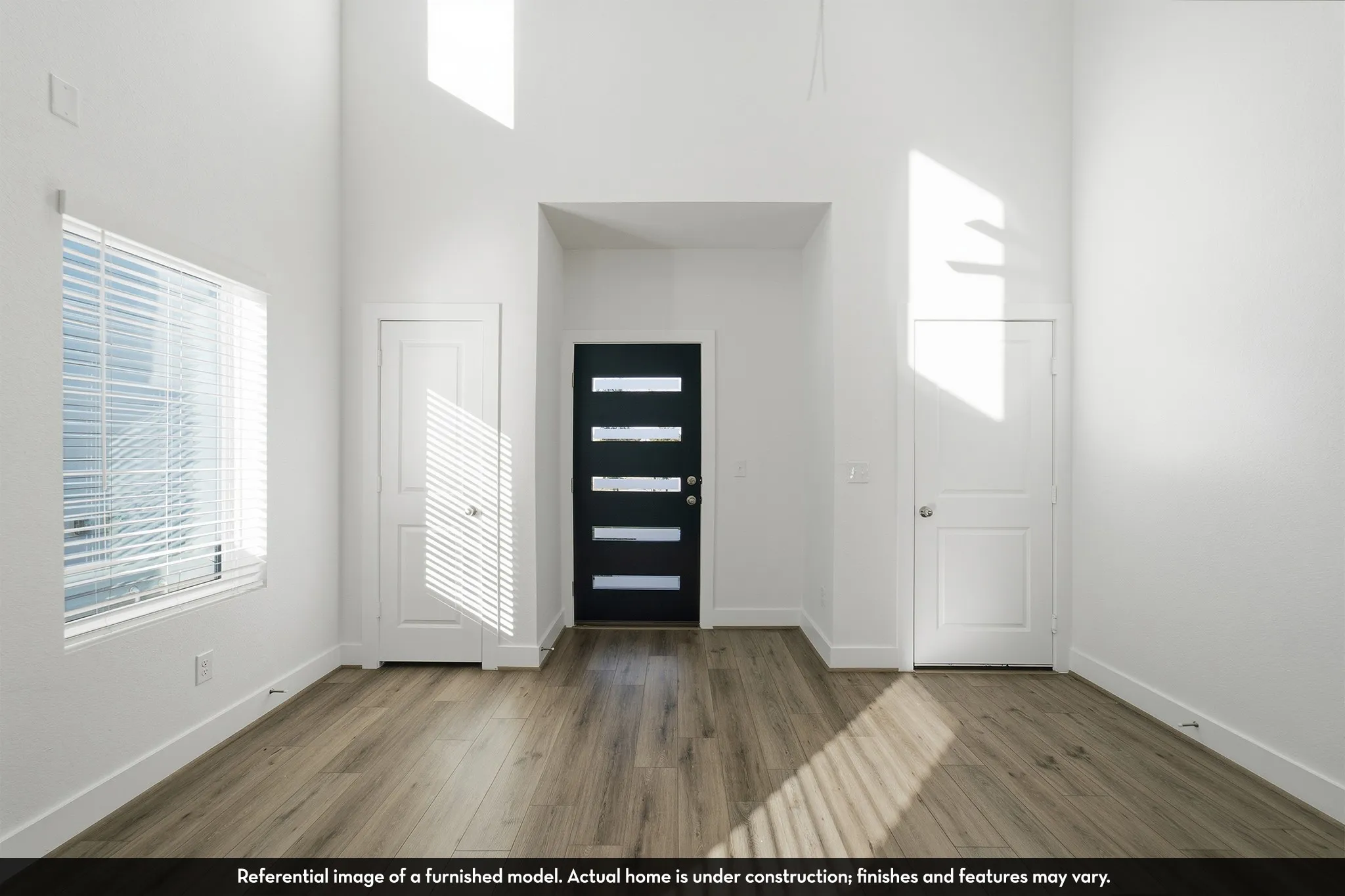 High-ceiling interior featuring wood-finish flooring, a multi-paneled front entry door, and large-scale windows with fitted blinds