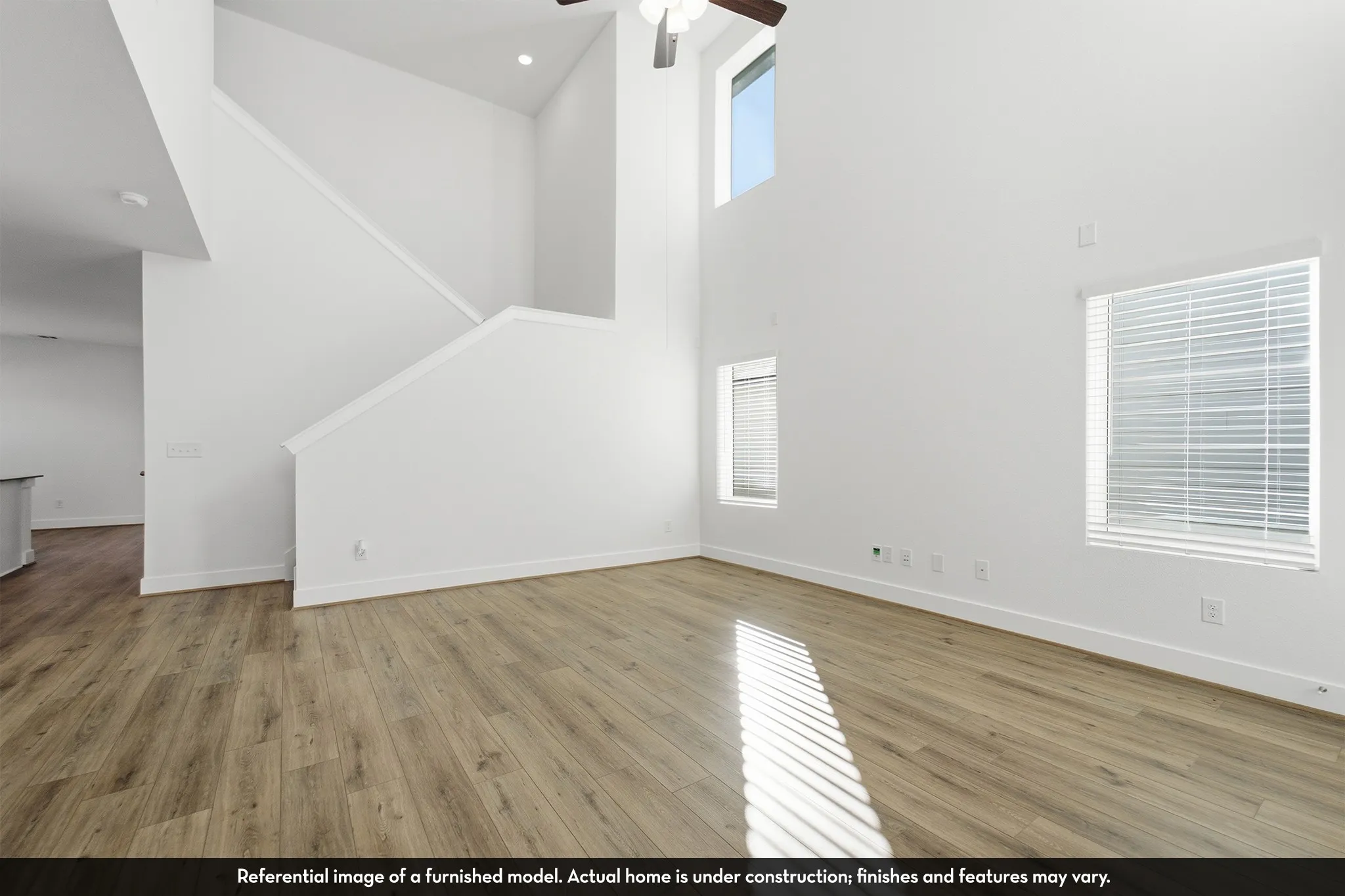 Open-concept interior featuring vaulted ceilings, wood-finish flooring, multi-level windows, and a ceiling fan with integrated light fixture
