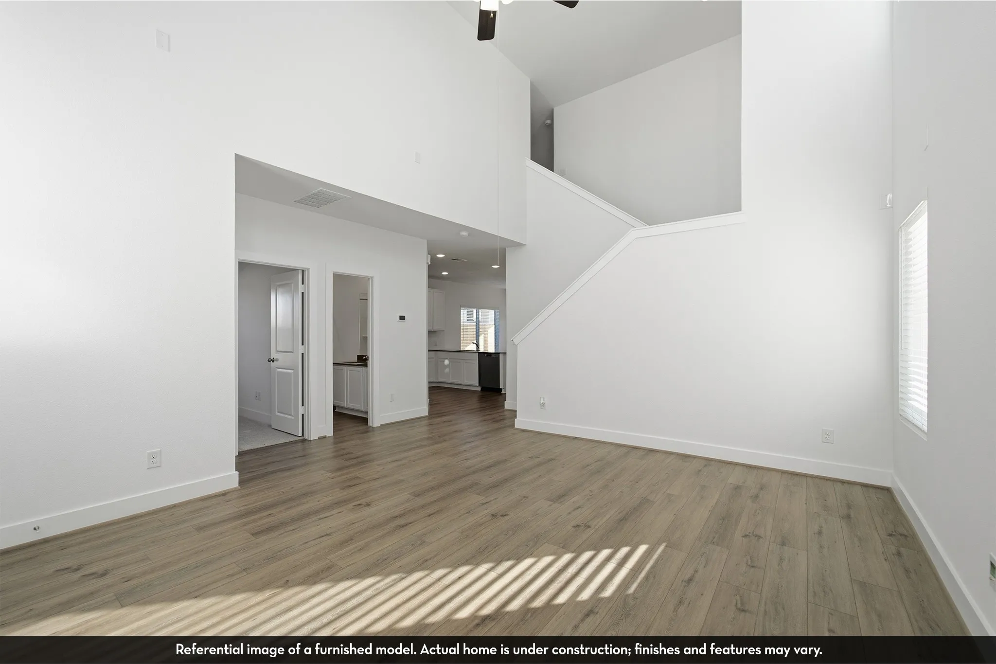High-ceiling interior featuring wood-finish flooring, a neutral color palette, and a staircase with a built-in railing