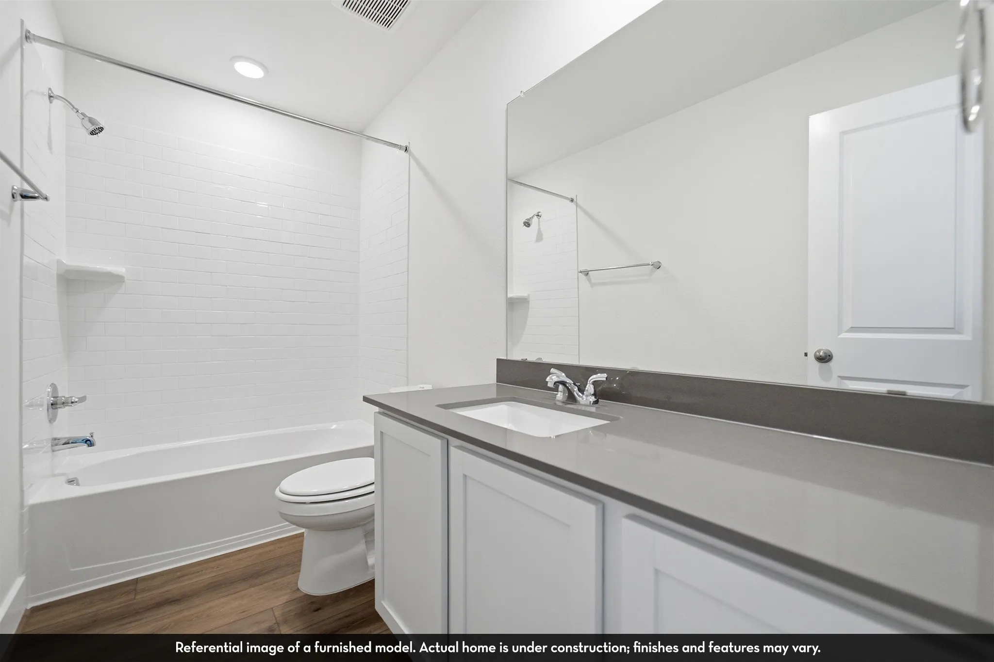 Bathroom featuring a vanity with a solid-surface countertop, an undermount rectangular sink, wood-finish flooring, a full-width wall mirror, and a tub-shower combination with tiled walls