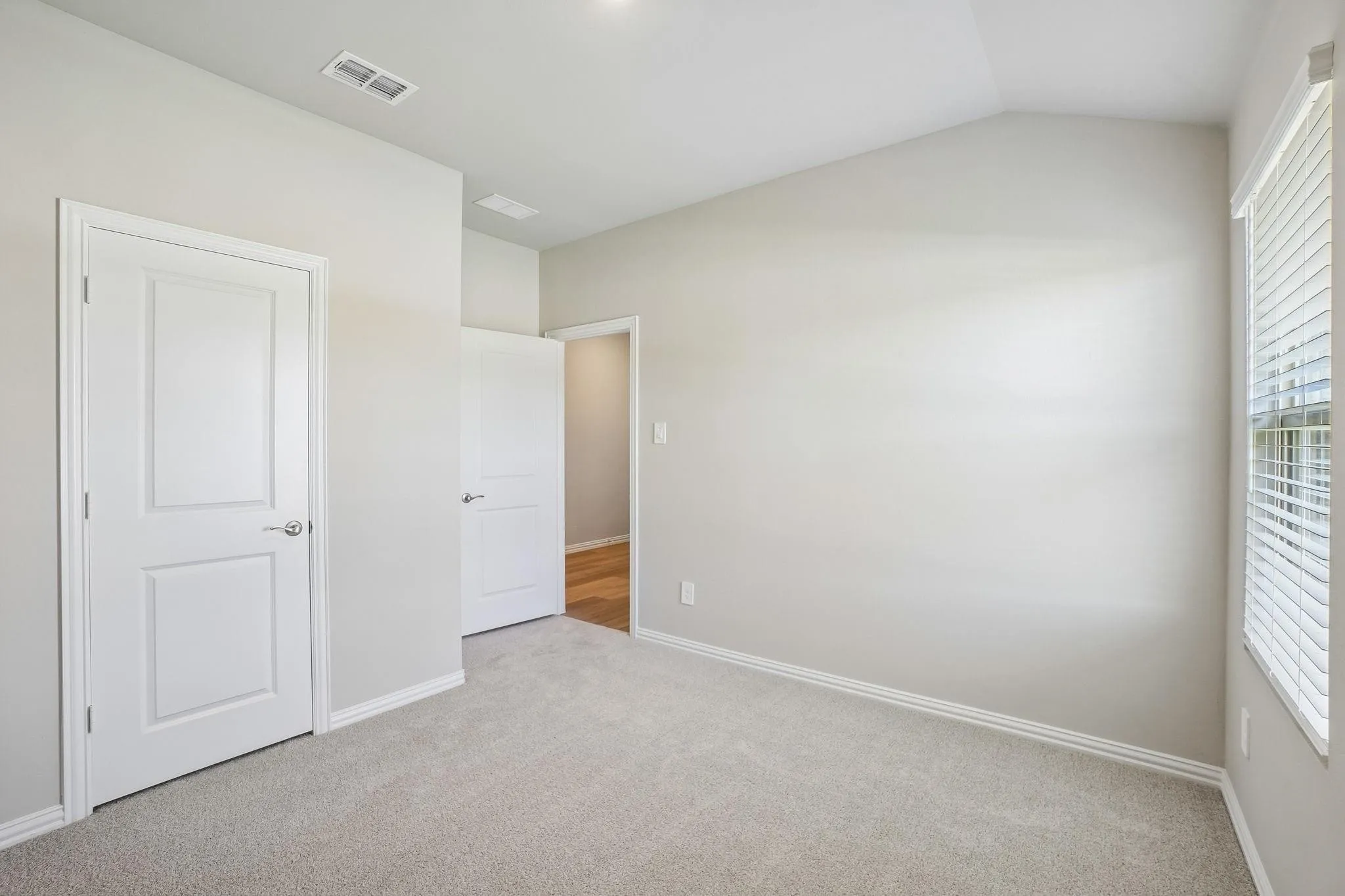Room featuring a vaulted ceiling, neutral wall tones, carpeted flooring, and a window with horizontal blinds