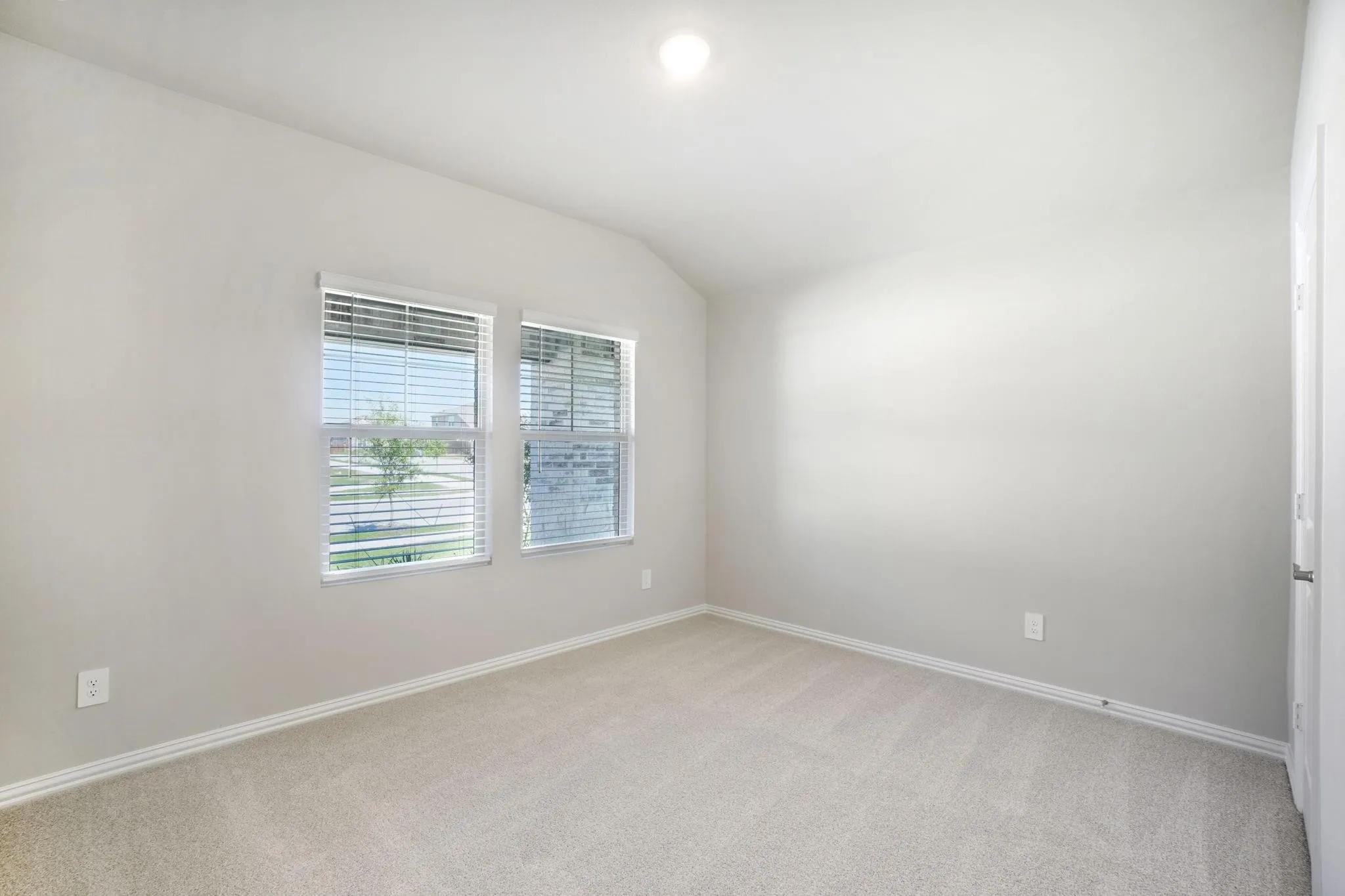 Neutral-toned interior space featuring a vaulted ceiling, wall-to-wall carpeting, and dual windows with fitted blinds