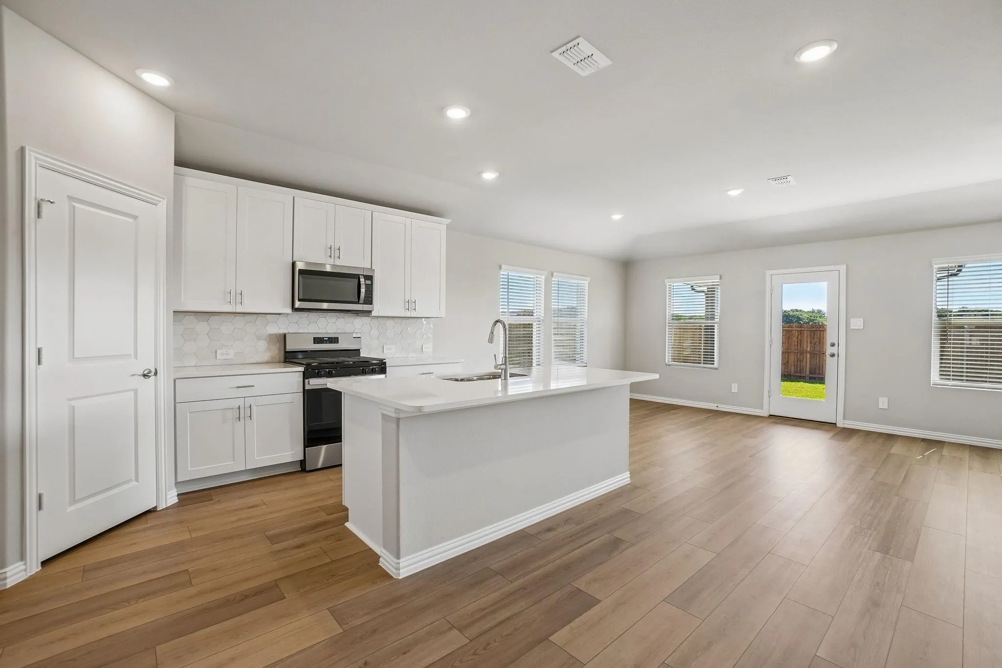 Kitchen featuring white shaker-style cabinetry, a central island with a solid surface countertop, stainless steel appliances, geometric tile backsplash, and wood-finish flooring