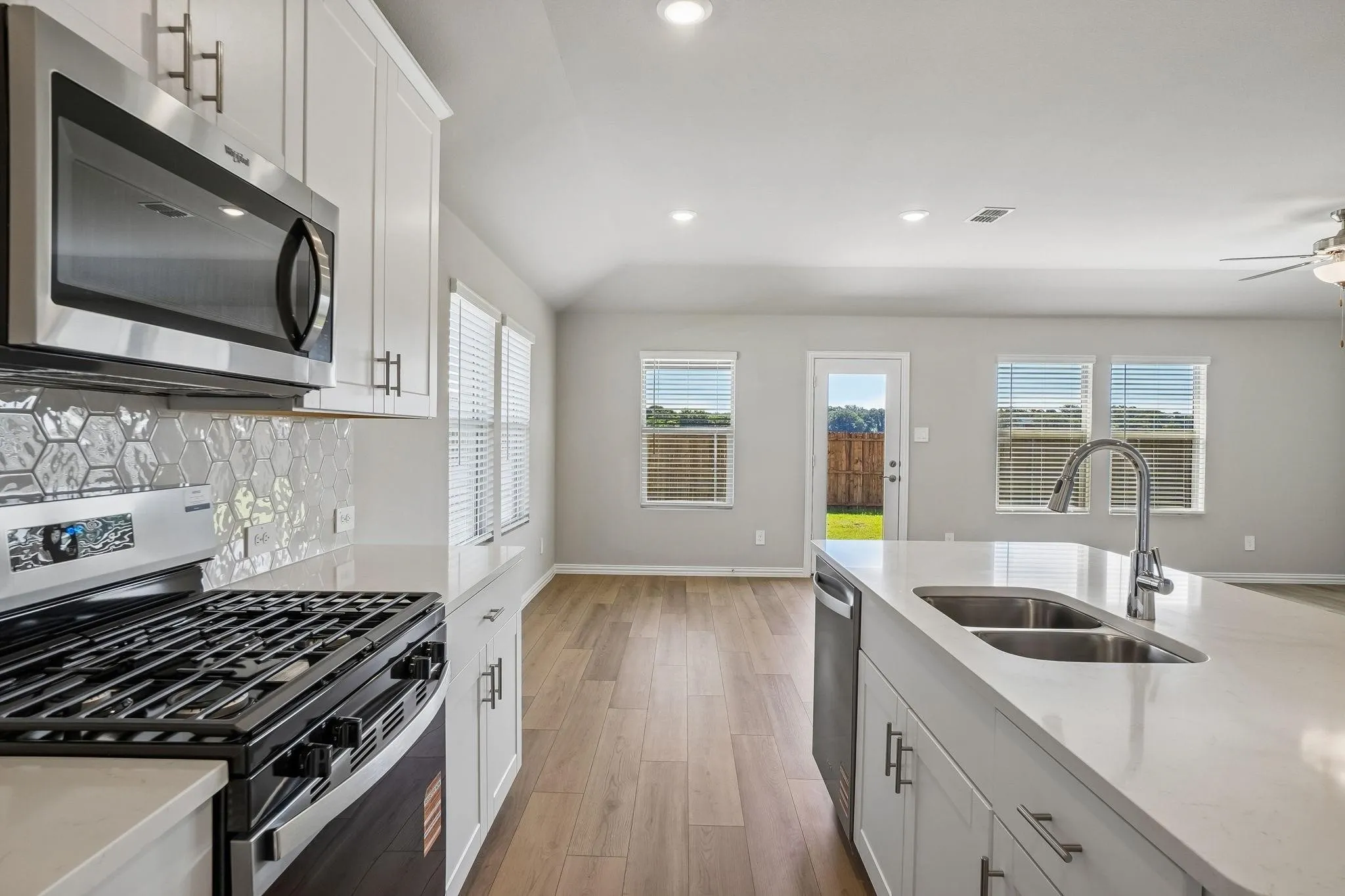 Kitchen featuring white shaker-style cabinetry, quartz countertops, a hexagonal tile backsplash, stainless steel appliances, and wood-finish flooring