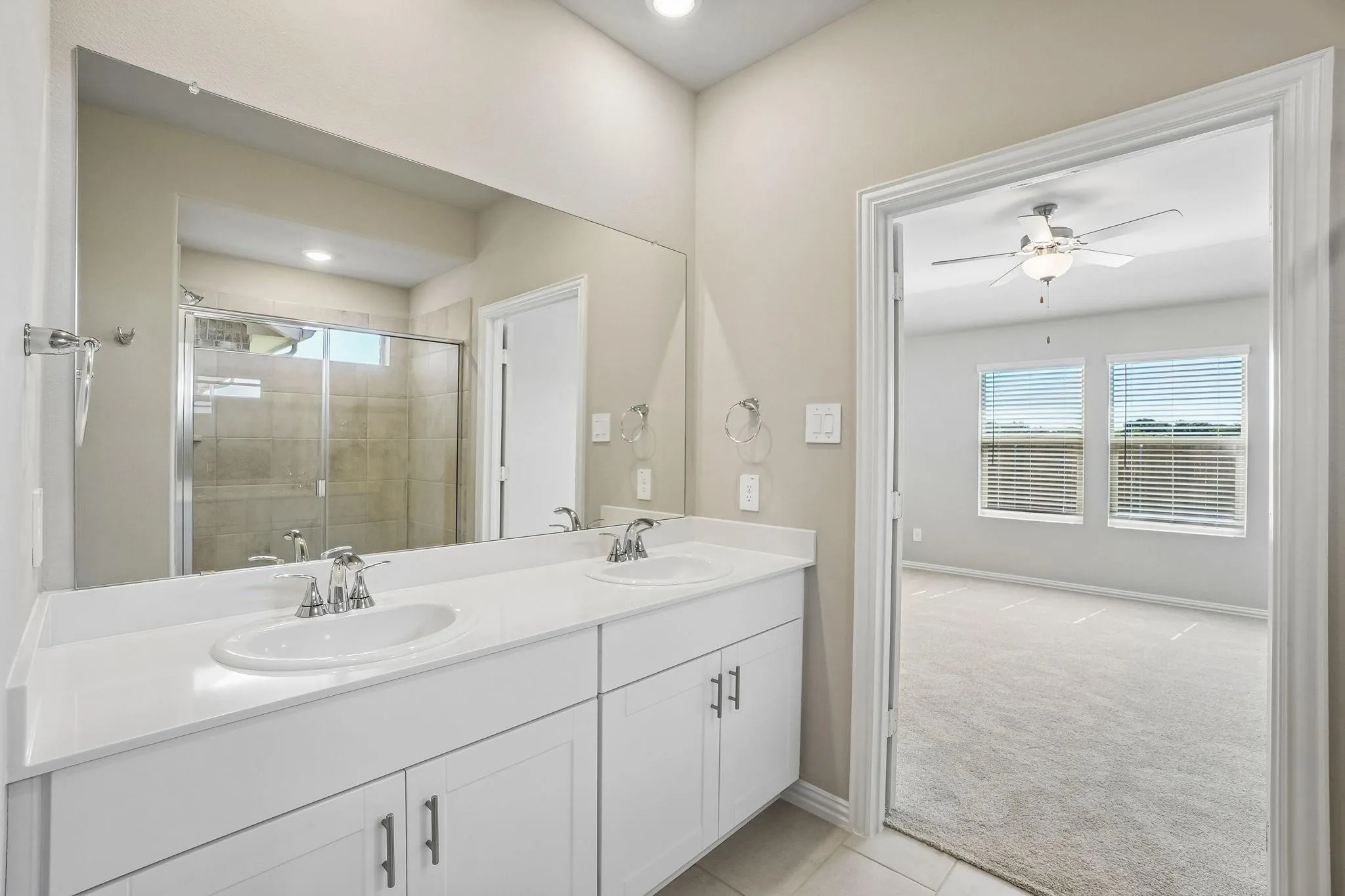 Dual-sink vanity with white cabinetry and solid-surface countertop, full-width mirror, and a glass-enclosed shower with tile surround