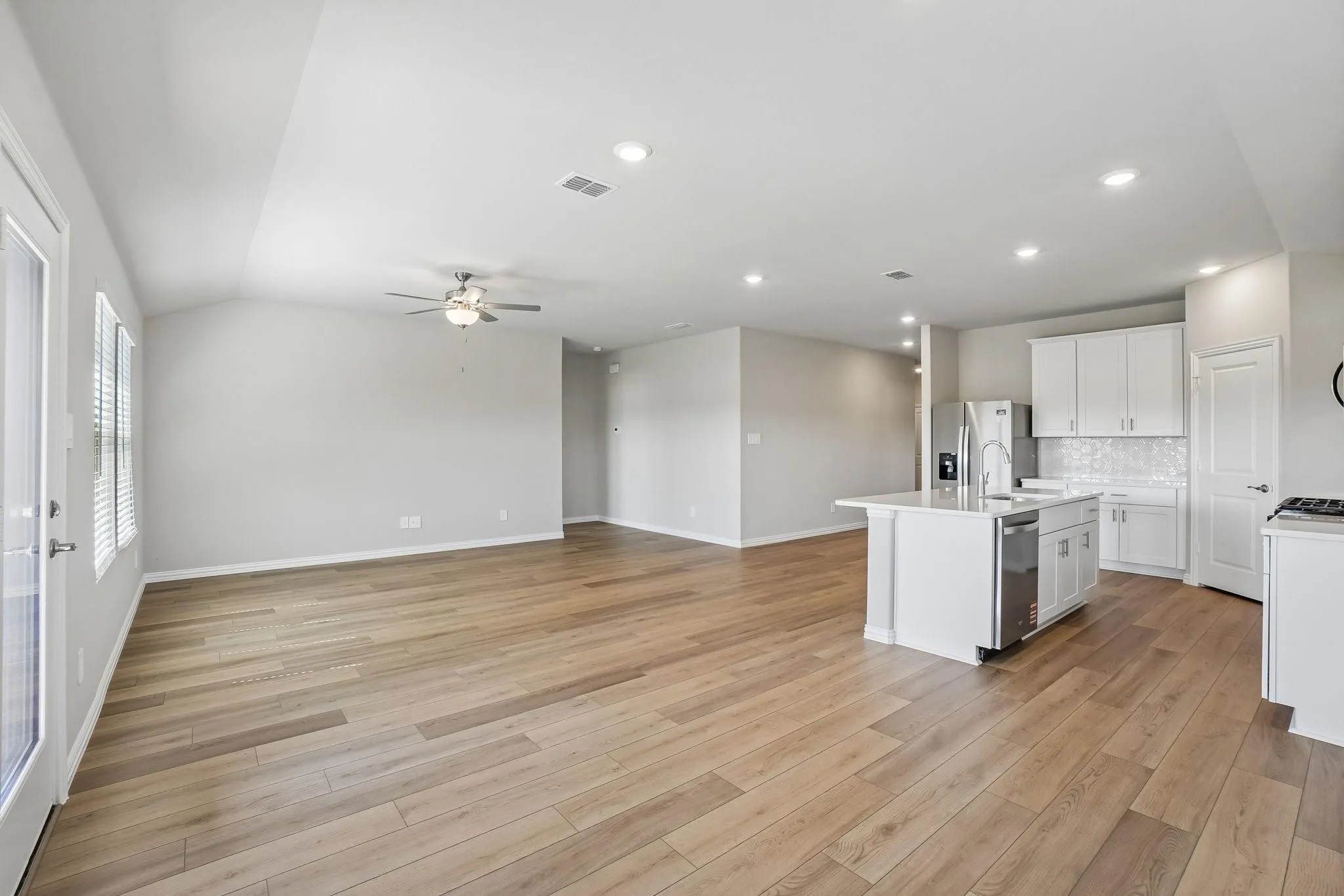 Open-concept interior featuring wood-finish flooring, recessed lighting, a vaulted ceiling with a central fan, and a kitchen with white cabinetry and a central island