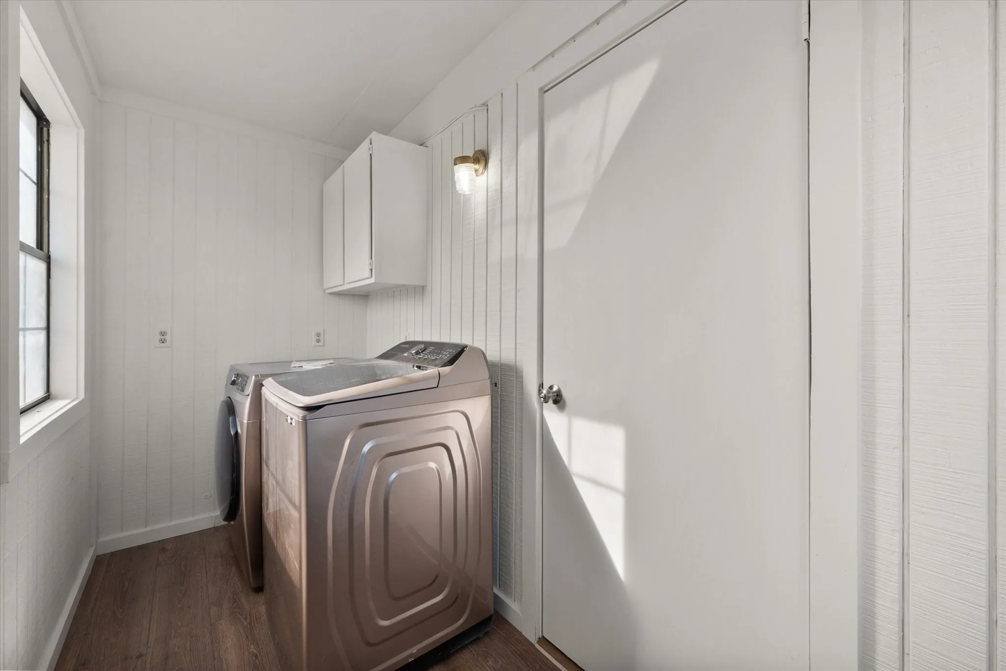 Laundry area featuring vertical plank wall paneling, wood-finish flooring, and white upper cabinetry