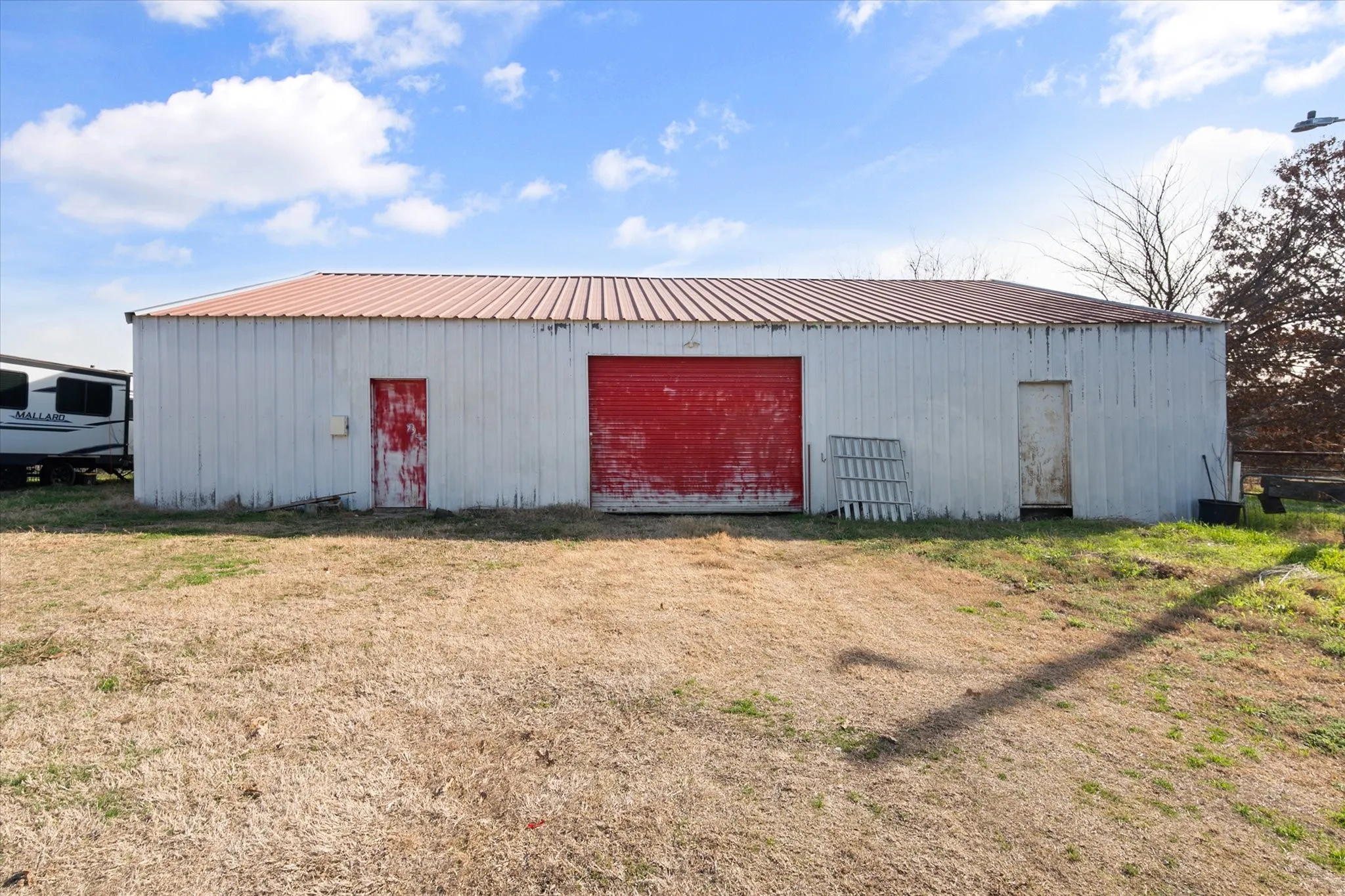 Metal-sided building featuring a red roll-up door, two entry doors, and a red metal roof