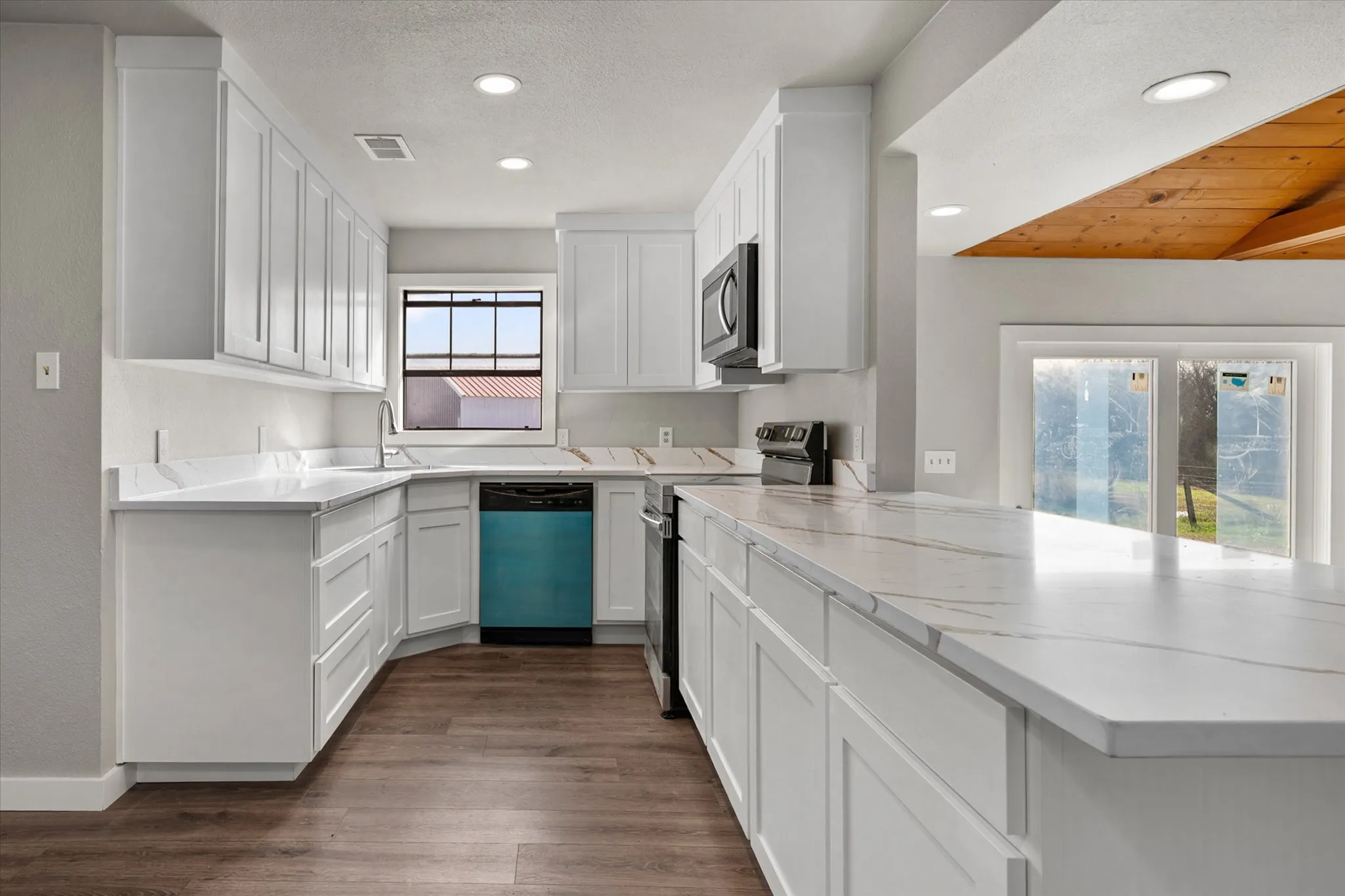 Modern kitchen featuring white shaker cabinetry, patterned countertops, wood-finish flooring, recessed lighting, and stainless steel appliances