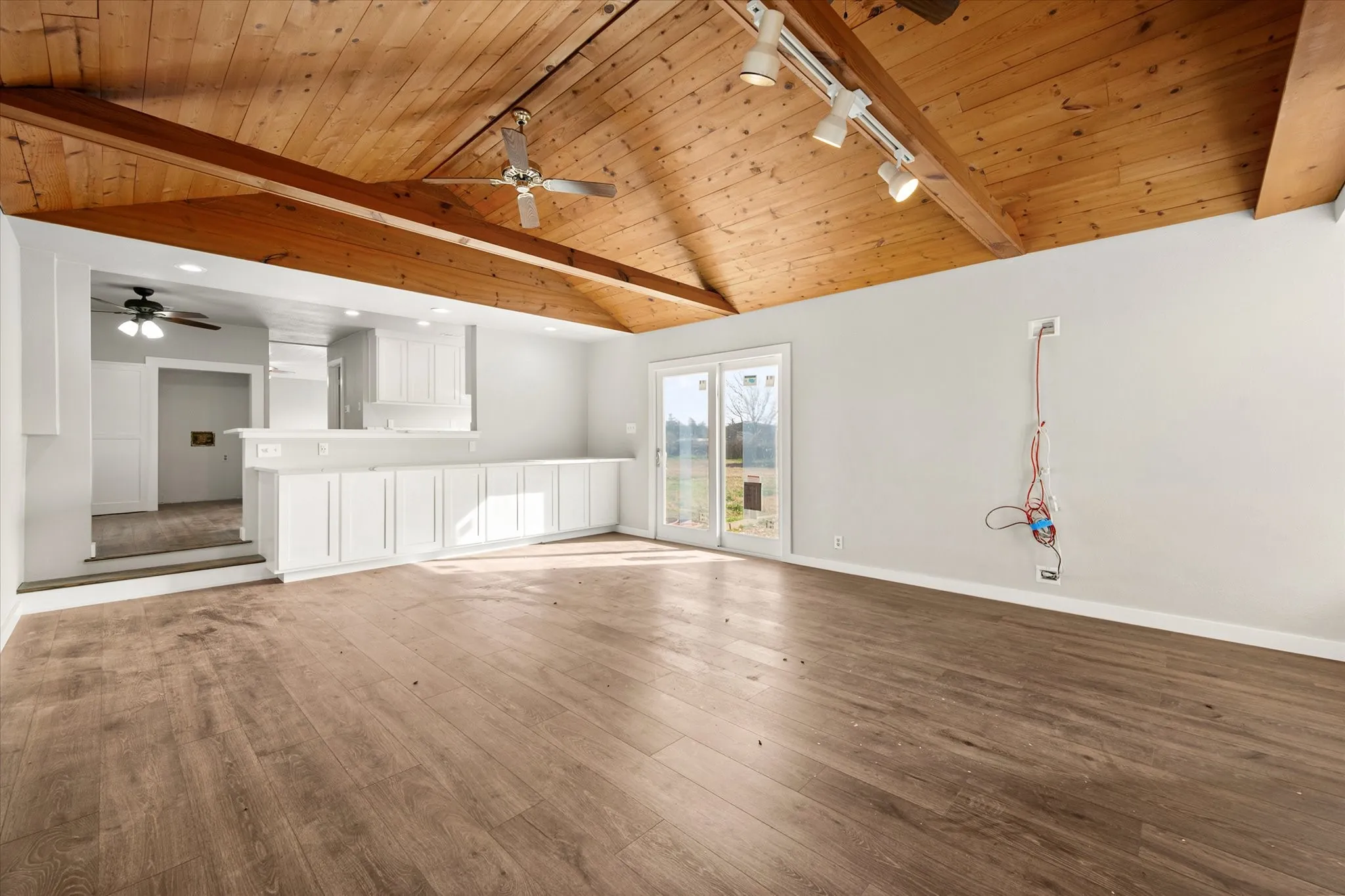 Vaulted wood-paneled ceiling with exposed beams, wood-finish flooring, white cabinetry, track lighting, and sliding glass doors