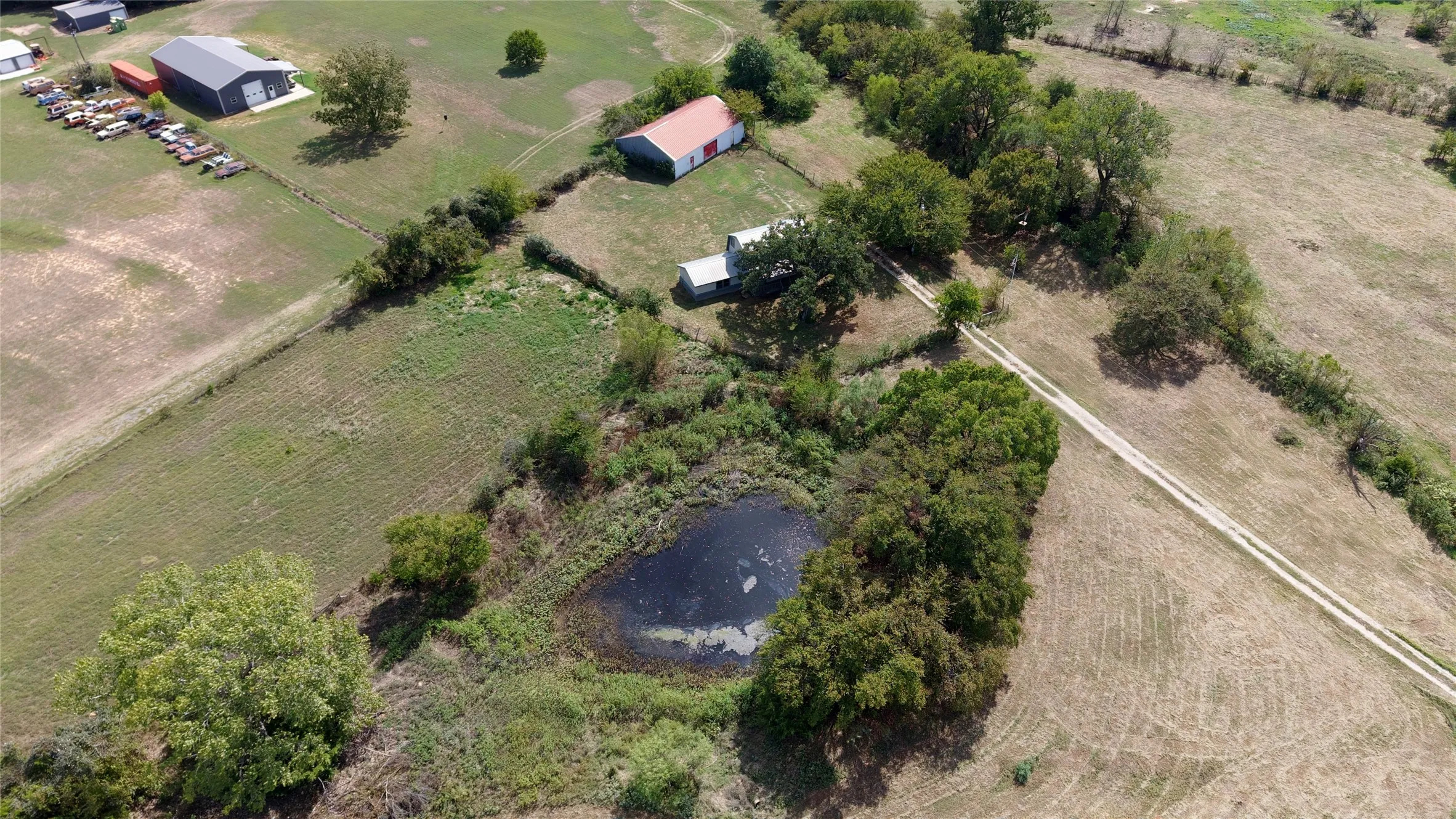 Expansive acreage featuring a pond, established trees, and multiple outbuildings