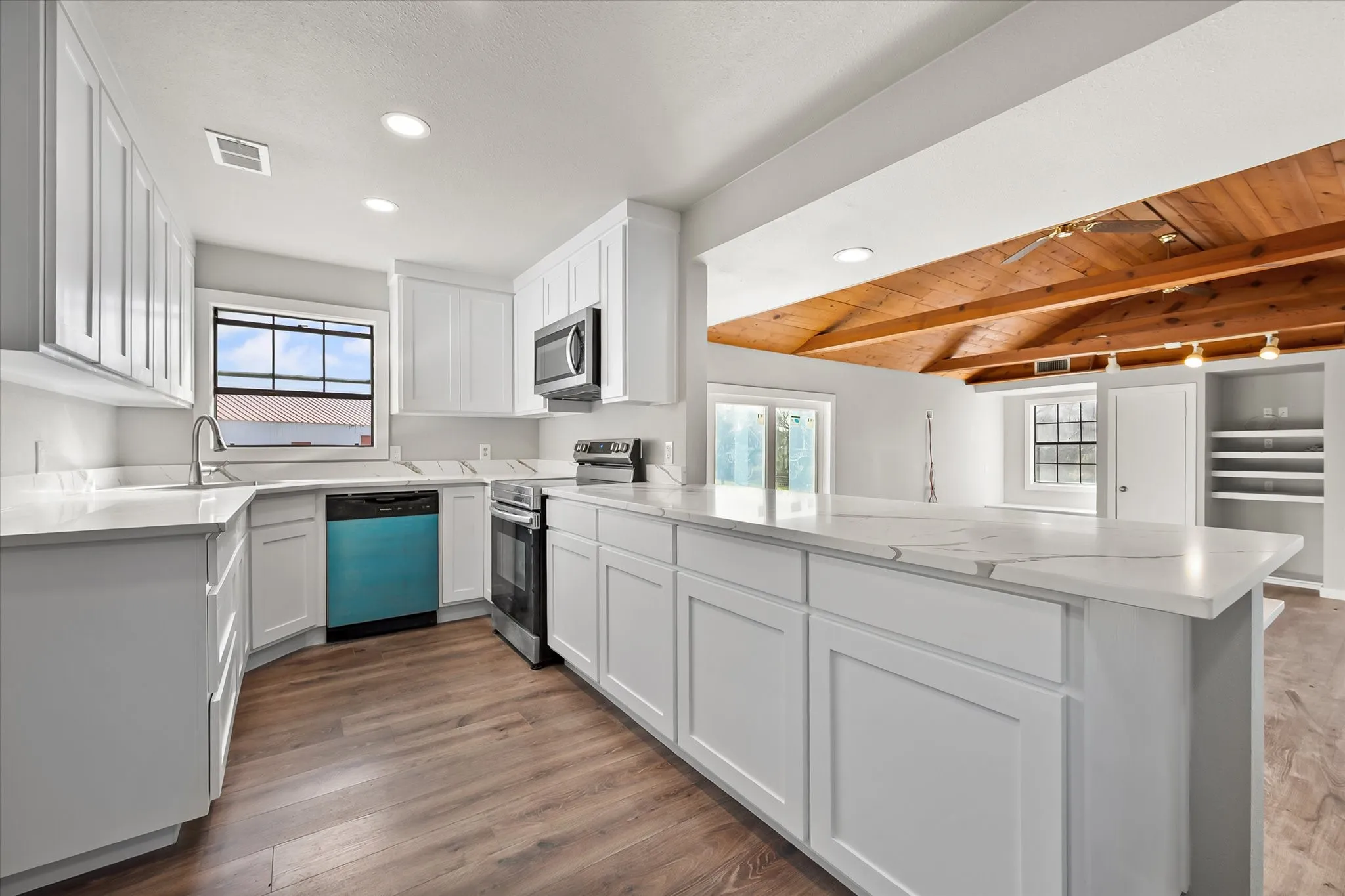 Kitchen featuring white cabinetry, light-toned countertops, wood-finish flooring, a stainless steel microwave, and a stainless steel range