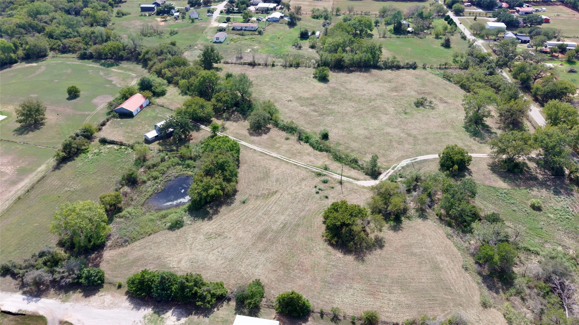 Expansive land parcel featuring open fields, scattered mature trees, a natural pond, and a barn