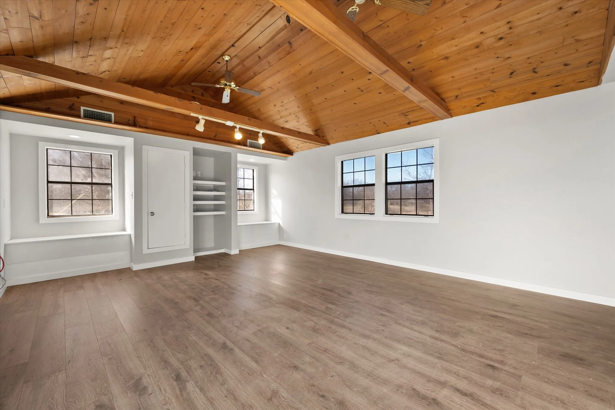 Vaulted wood-paneled ceiling with exposed beams, wood-finish flooring, built-in shelving, track lighting, and multiple windows