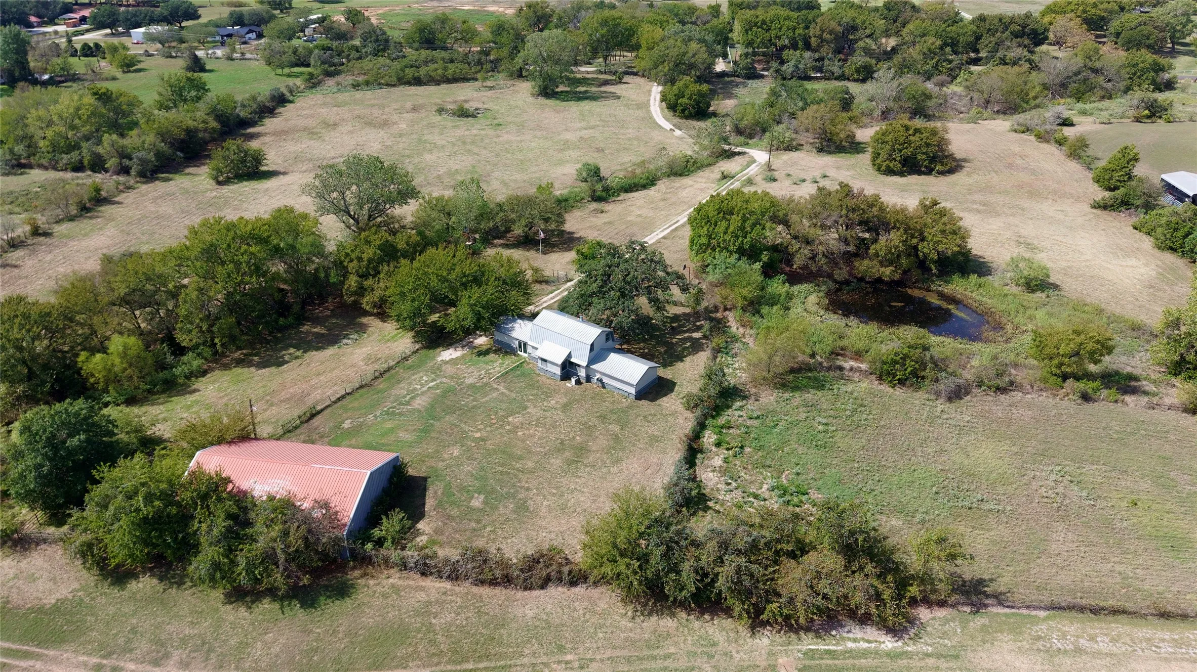 Expansive property featuring a dwelling, outbuilding with a red roof, natural pond, and mature trees