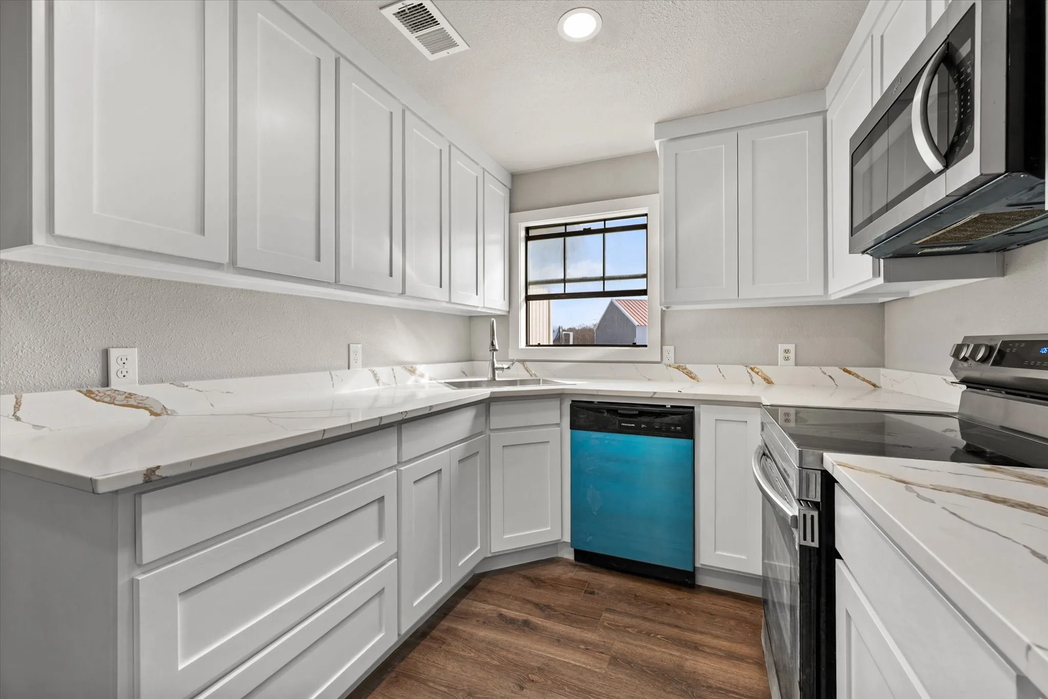 White shaker-style cabinetry, patterned countertops, stainless steel appliances, wood-finish flooring, and a single-basin sink with a pull-down faucet