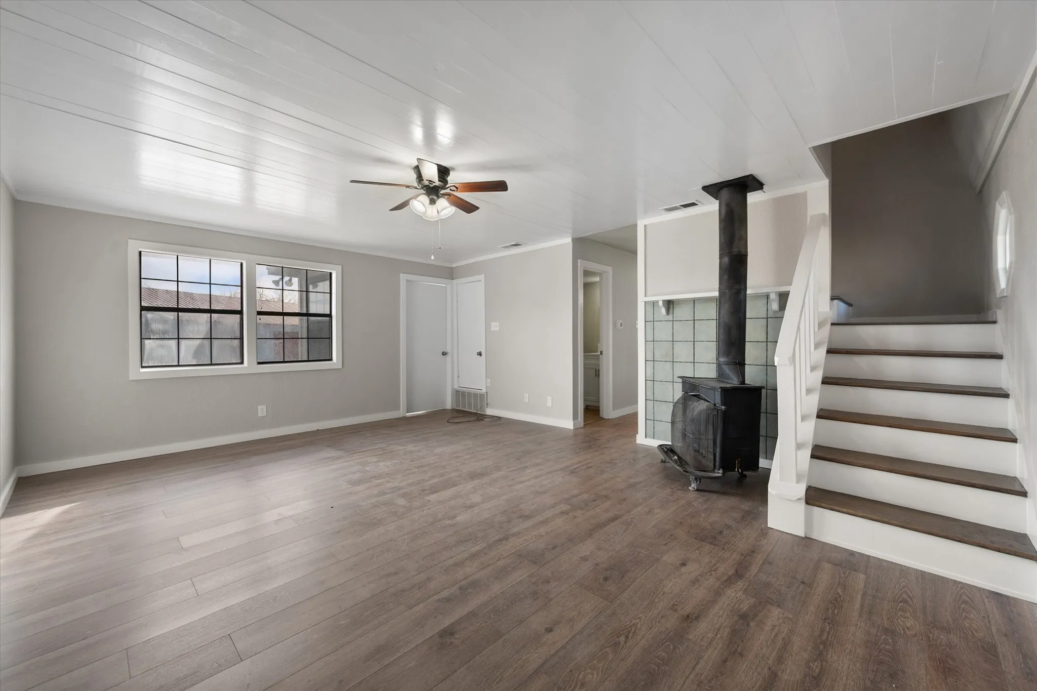 Spacious interior featuring wood-finish flooring, a ceiling fan, and a wood-burning stove with a glass block surround