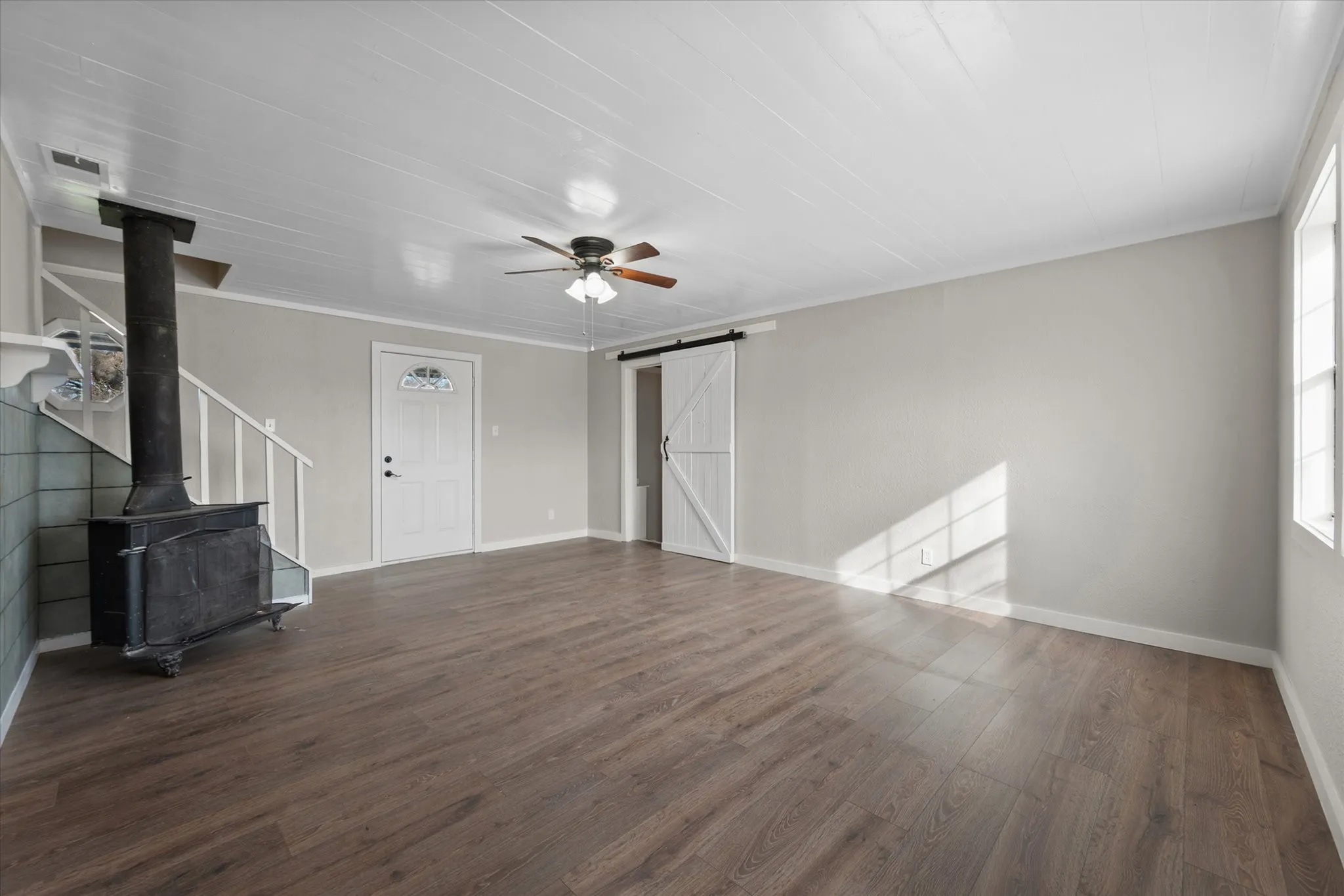 Wood-finish flooring, white paneled ceiling, ceiling fan with light fixture, white front entry door with decorative glass inlay, and a white barn door
