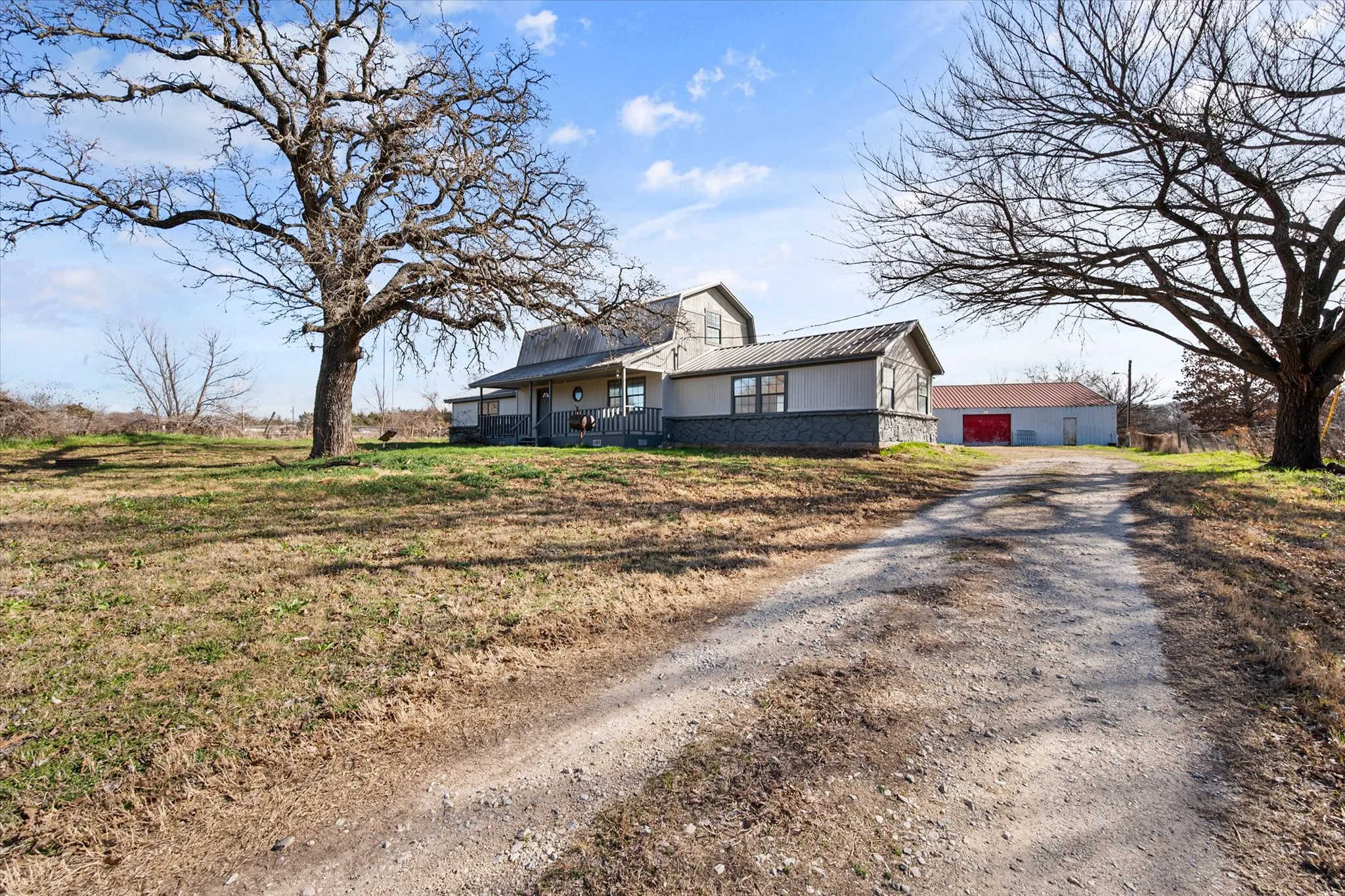 Two-story residence featuring a covered front porch, a gravel driveway, and a detached building with a red door