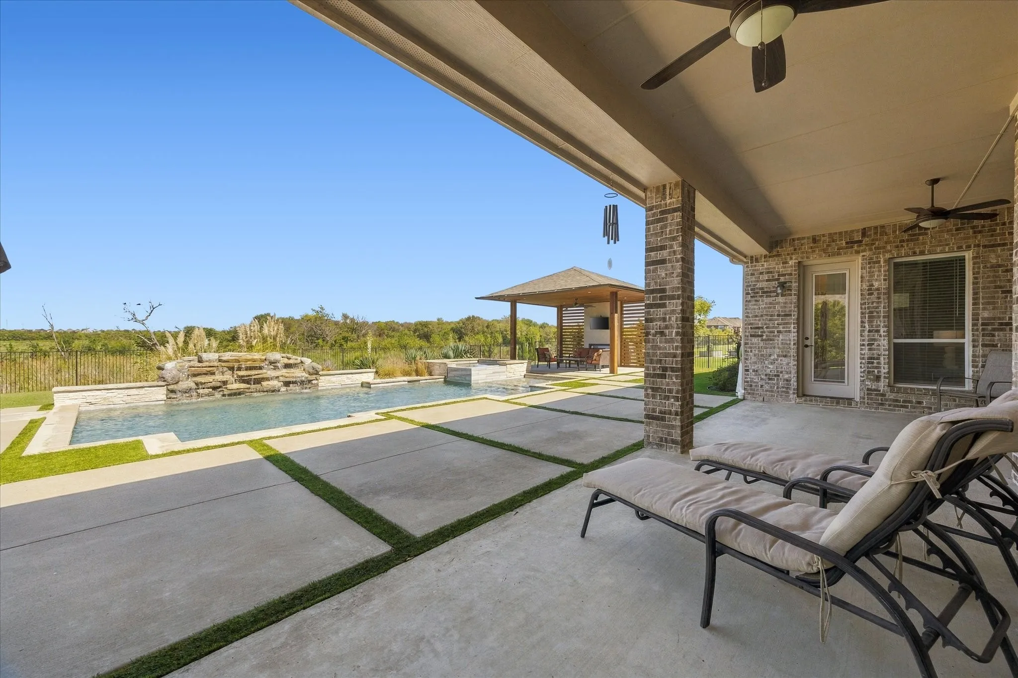 Covered patio with brick columns and ceiling fans, featuring a geometric concrete patio with artificial turf accents