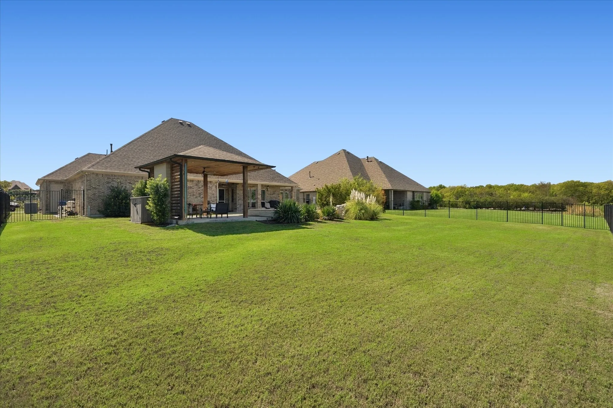 Expansive rear lawn featuring a covered patio, brick exterior, and dark-finish perimeter fencing