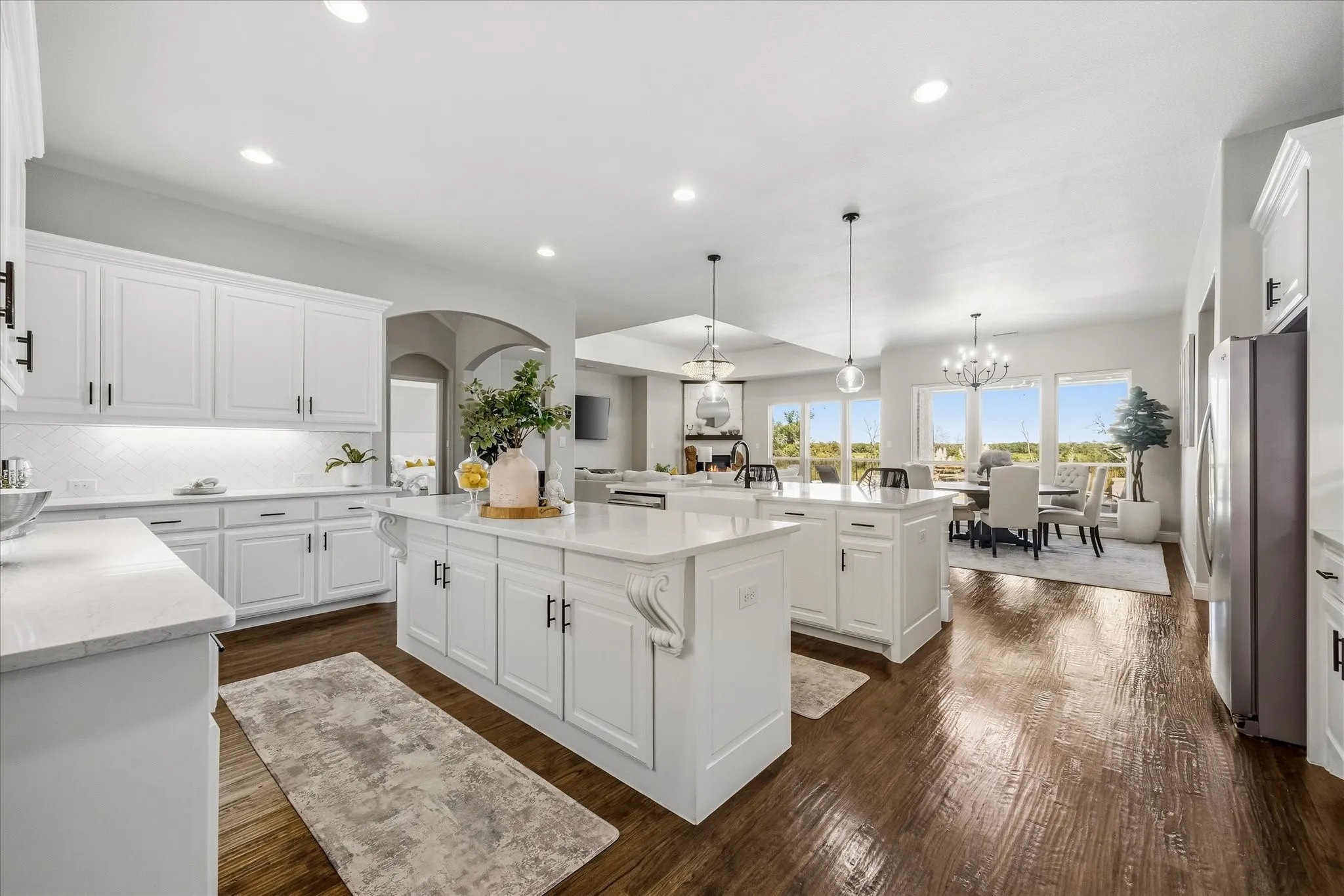 Spacious kitchen with dual islands, white cabinetry, integrated stainless steel appliances, and wood-finish flooring