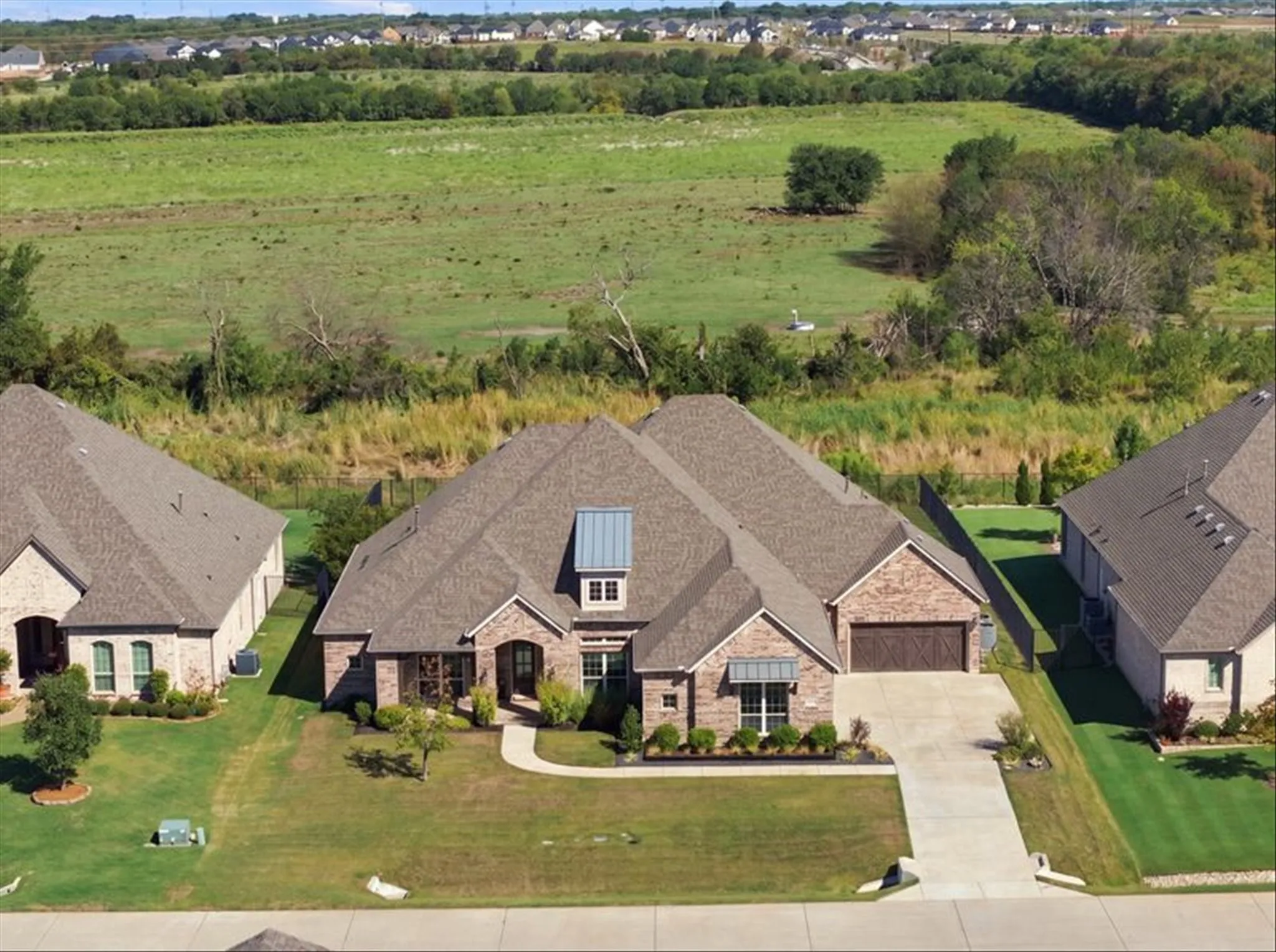 Brick exterior with stone accents, covered entry, attached garage, concrete driveway, and manicured landscaping