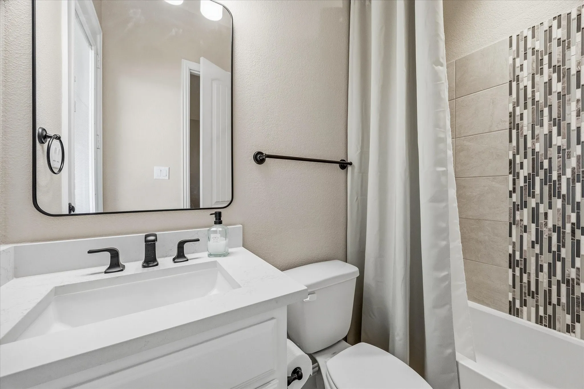 Vanity with a white countertop and rectangular sink, matte black faucet, and a framed mirror
