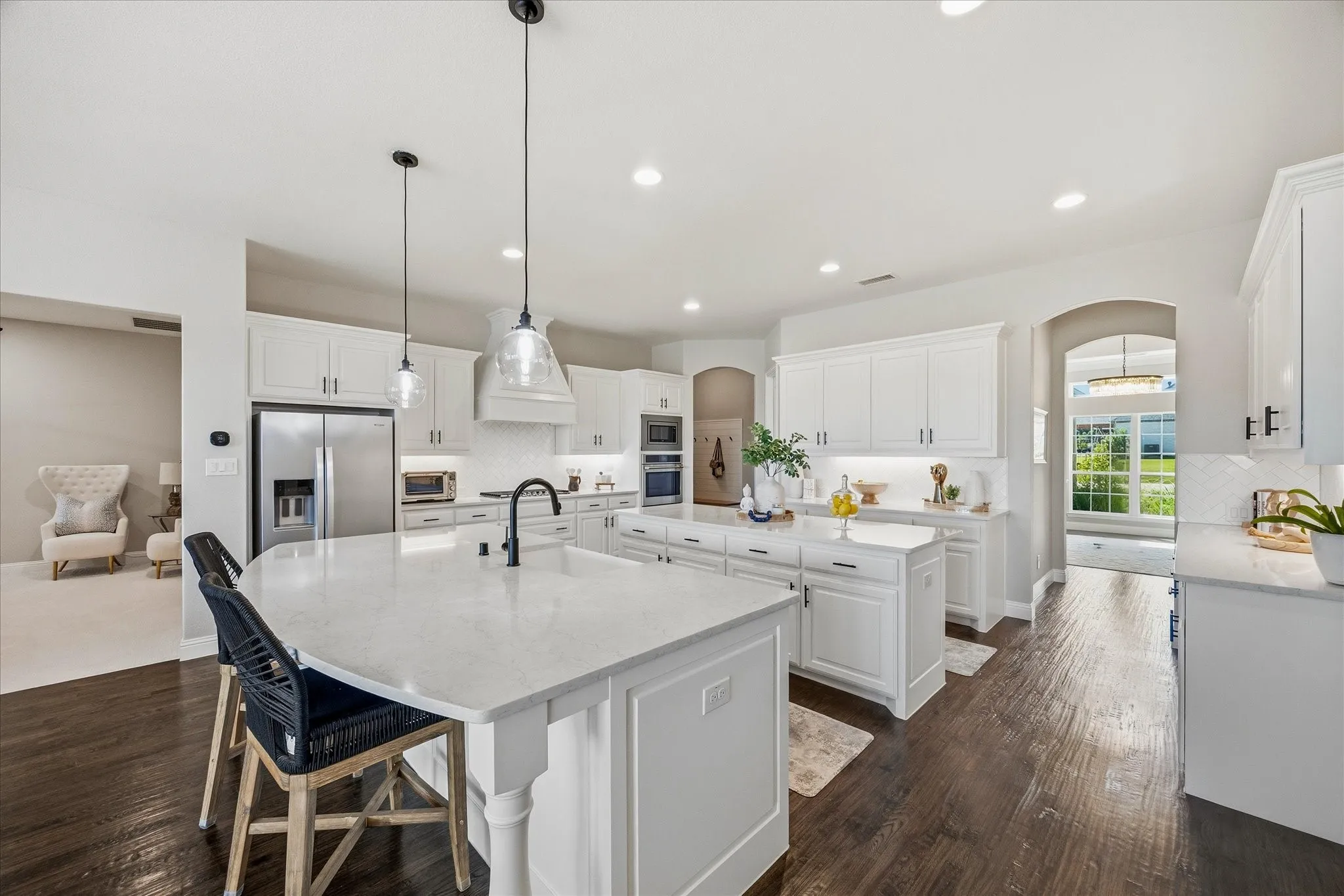 Kitchen featuring dark wood-finish flooring, white cabinetry, integrated stainless steel appliances, and two islands with light-colored countertops