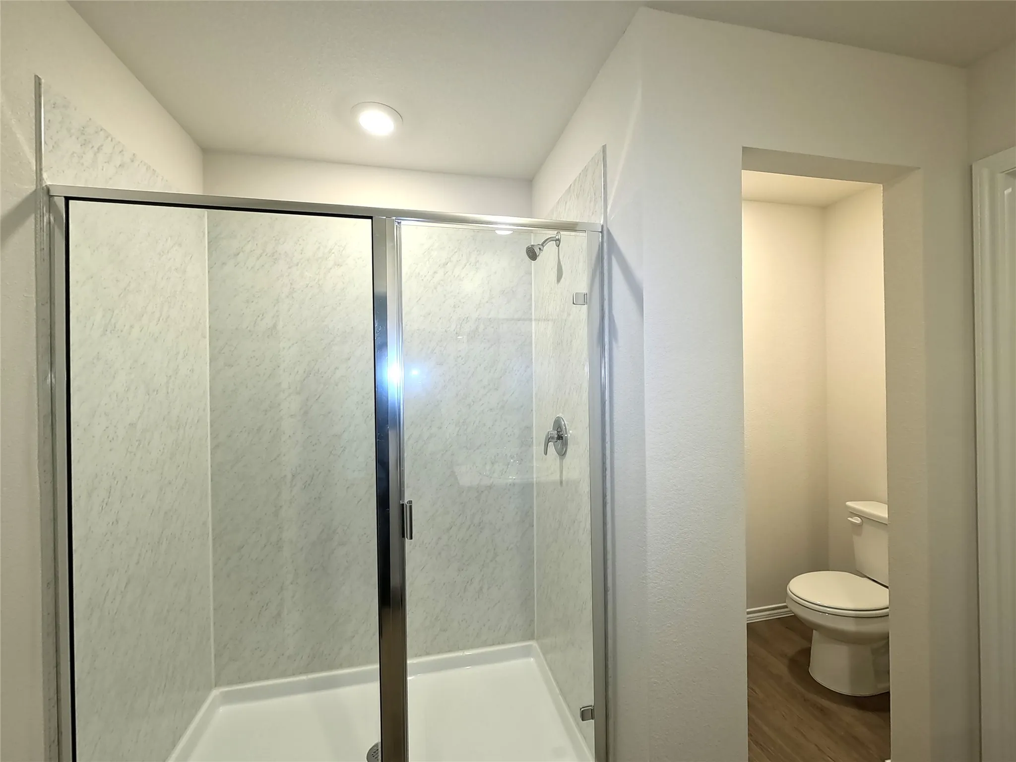Shower stall featuring a glass enclosure with chrome trim and stone-patterned surround, recessed lighting, and wood-finish flooring