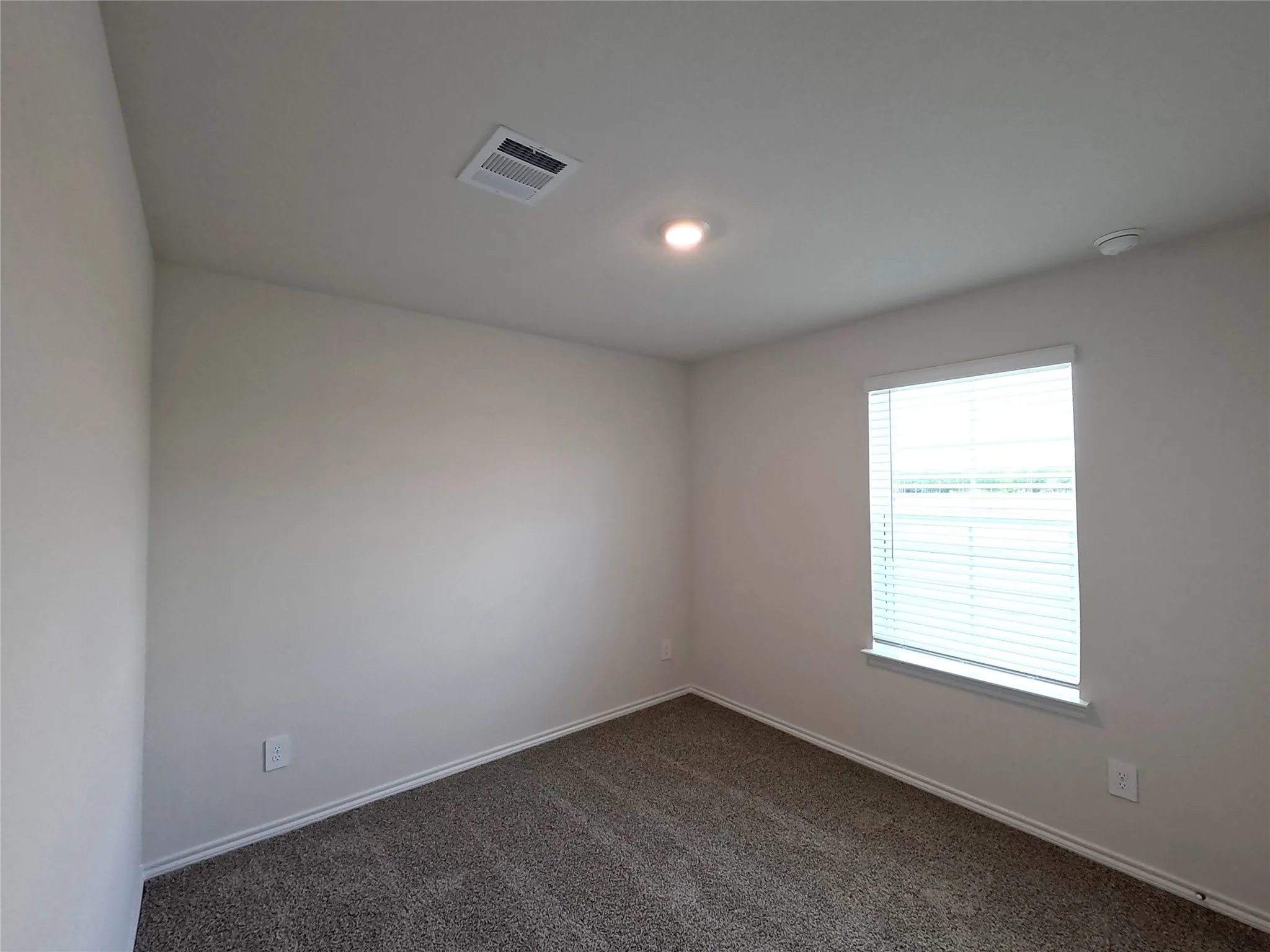 Neutral-toned interior room featuring wall-to-wall carpeting, a single-pane window with white horizontal blinds, and a recessed ceiling light