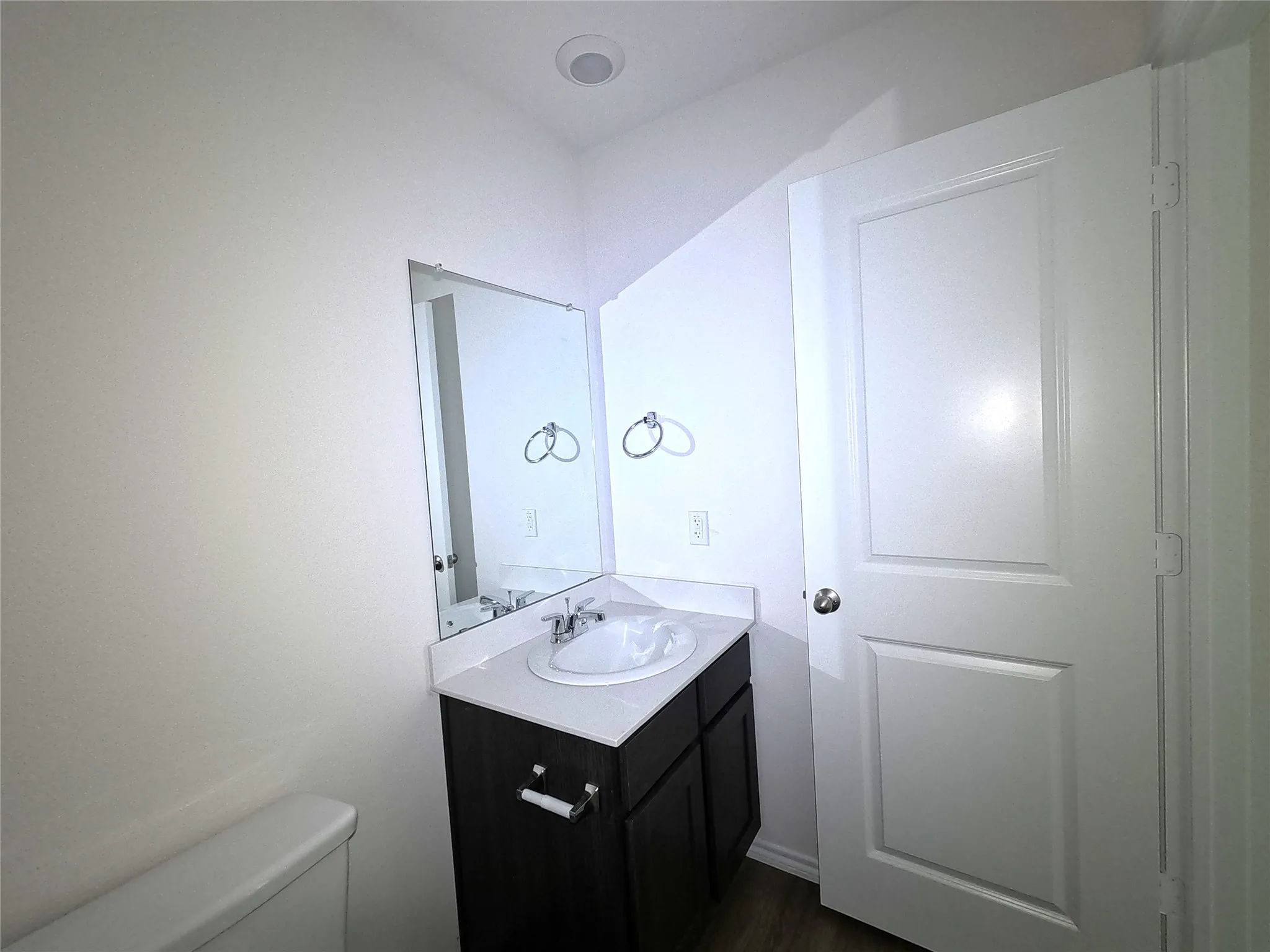 Vanity cabinet with dark wood-finish cabinetry, white countertop, integrated basin, wall-mounted mirror, and chrome hardware
