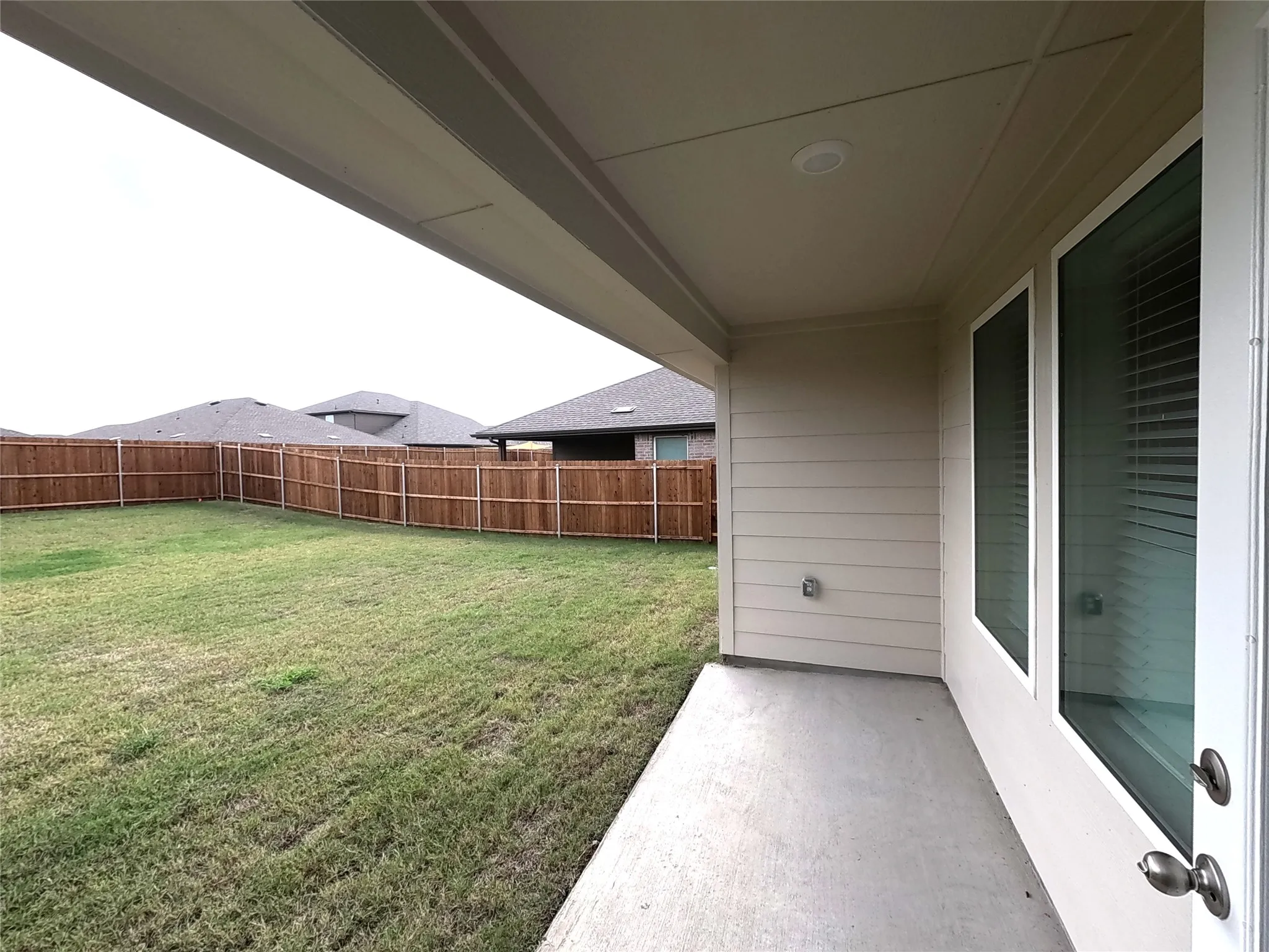 Covered concrete patio with recessed lighting, horizontal lap siding, and fenced backyard