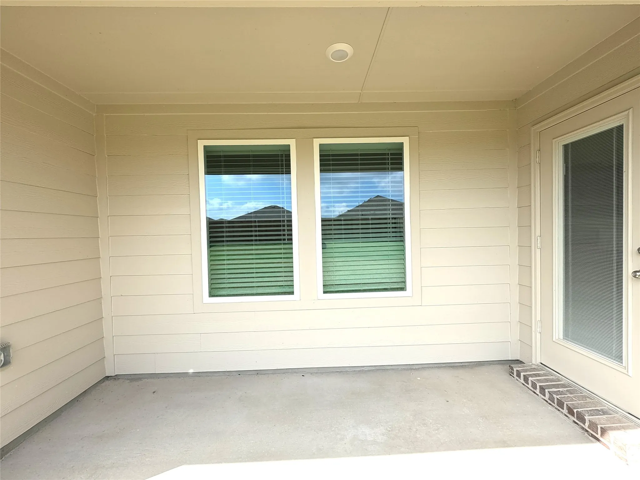 Covered patio featuring concrete flooring, horizontal siding, dual windows, and an exterior door with inset glass